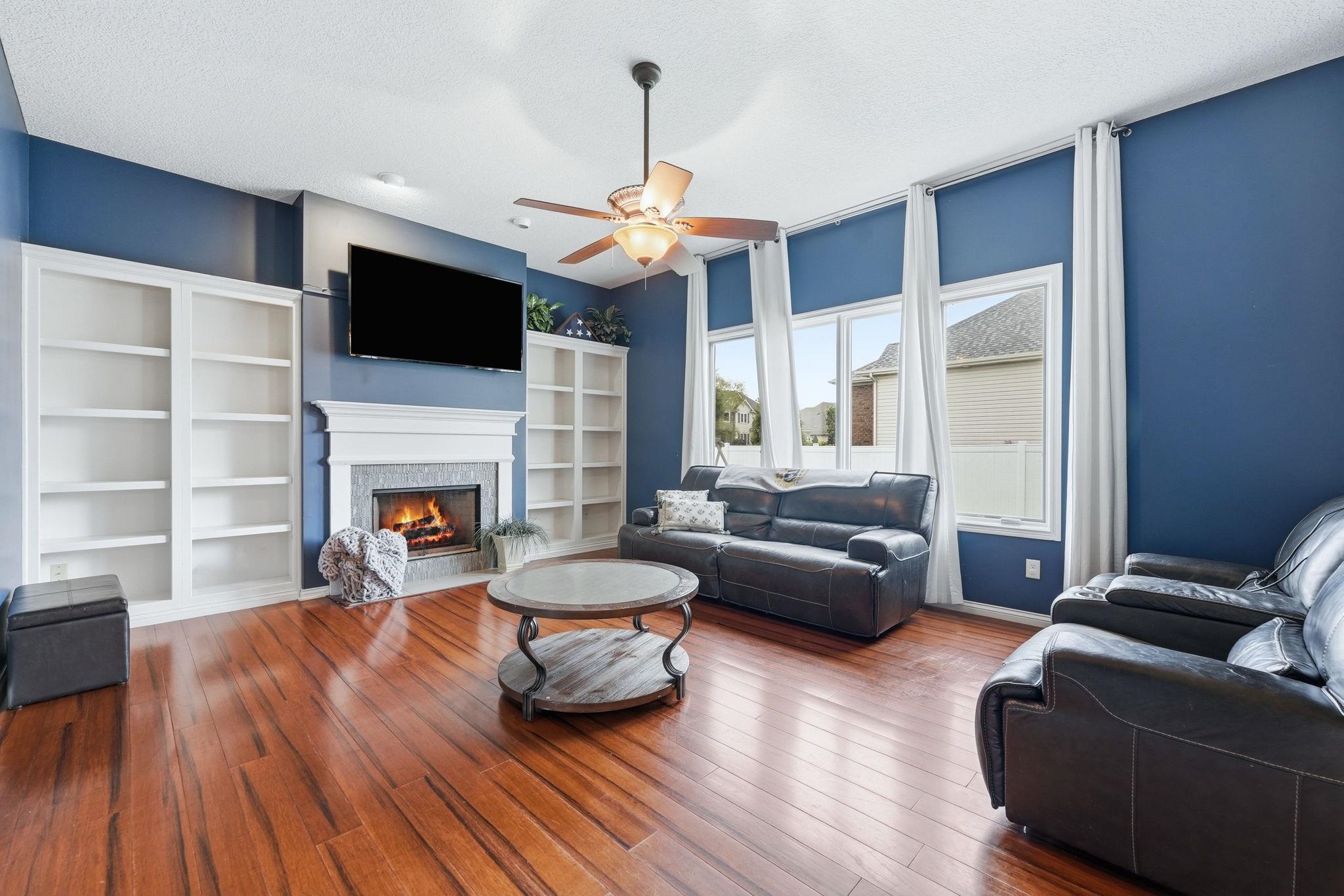 Living area featuring rich wood-finish flooring, a built-in fireplace with a decorative mantel and stone surround, and surrounding built-in shelving