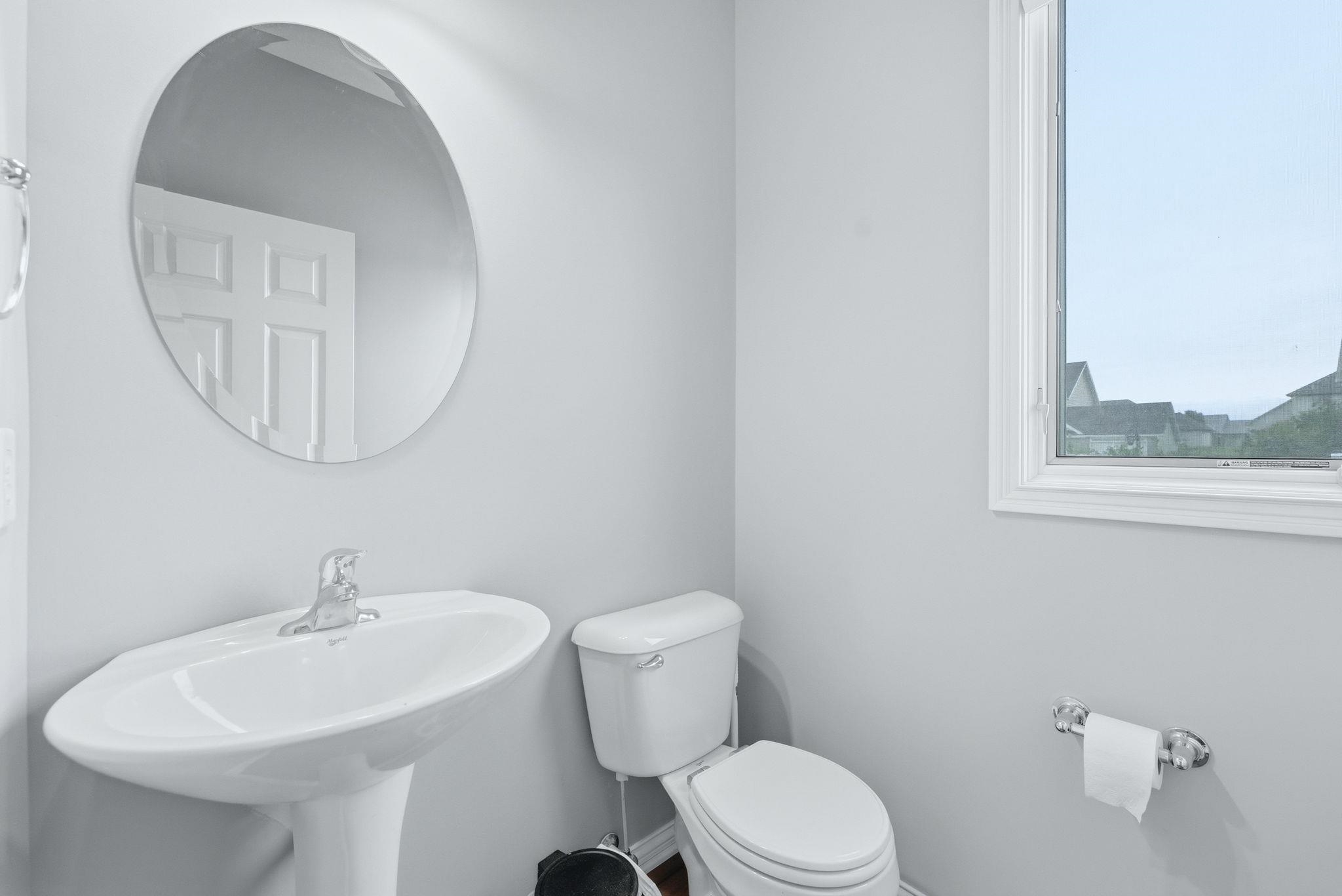 Bathroom featuring a pedestal sink with chrome faucet, circular wall mirror, and a white framed window
