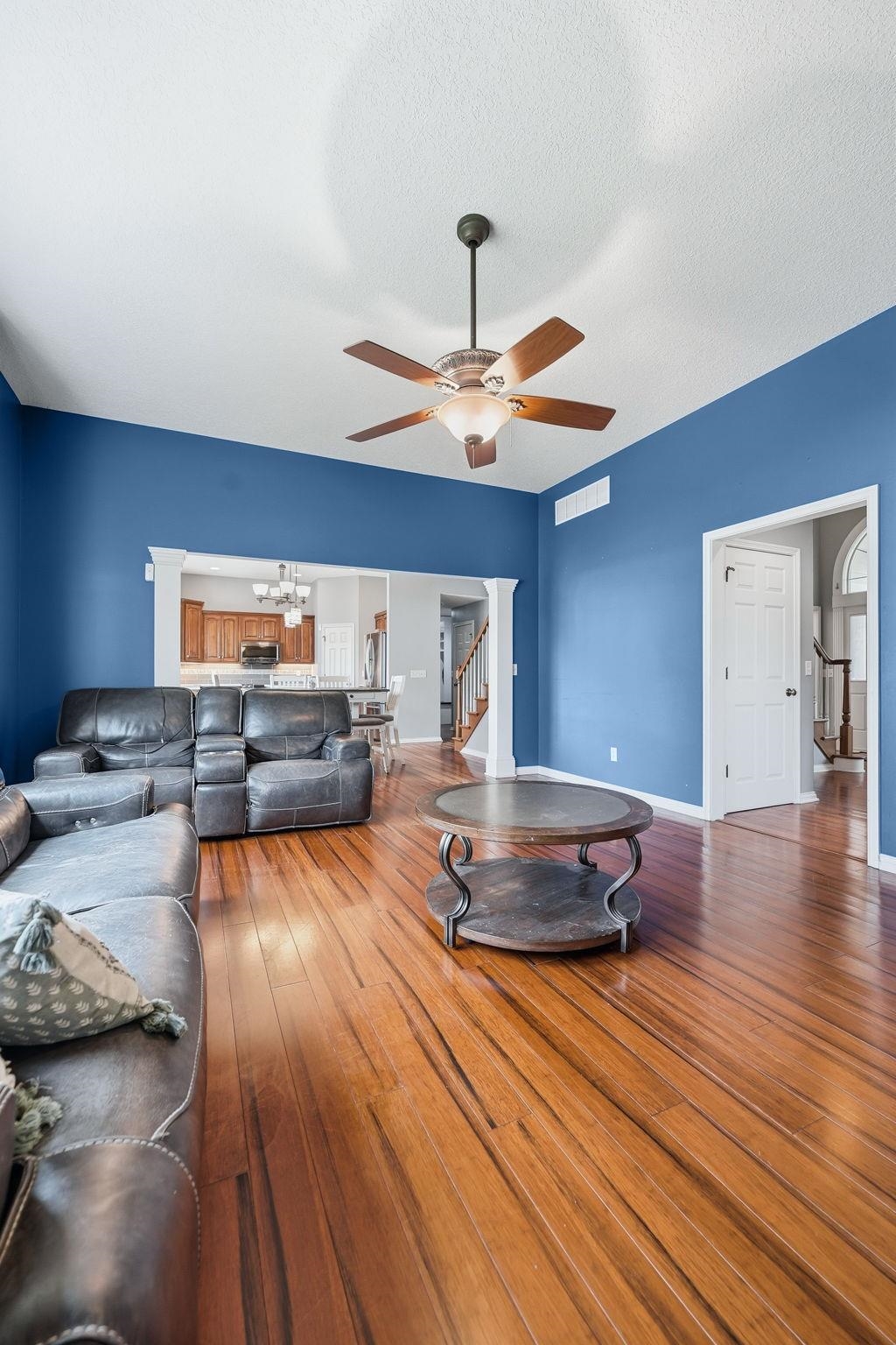 Spacious living area featuring polished wood-finish flooring, a contemporary ceiling fan, and vibrant wall finishes