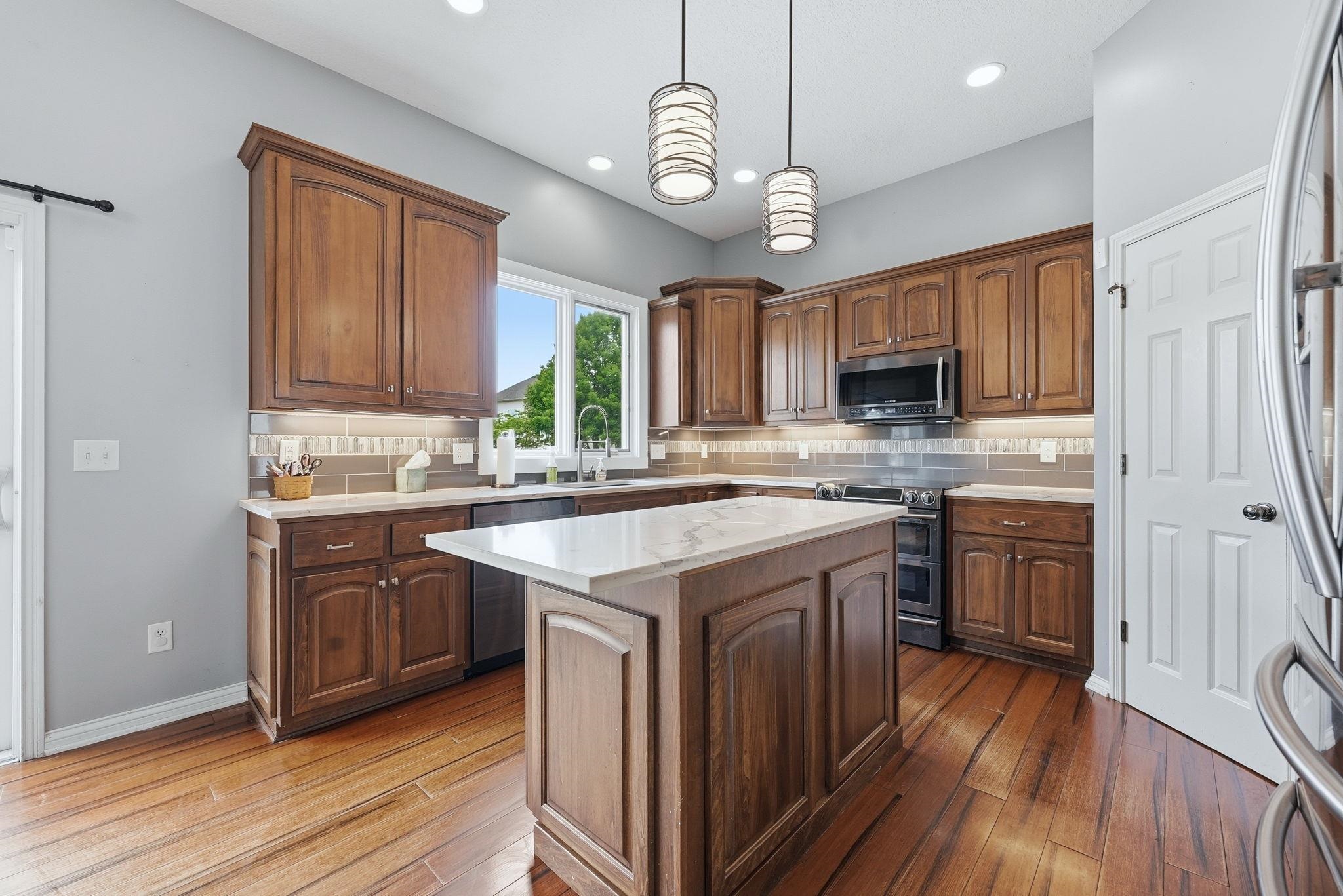 Kitchen featuring a central island with a light-toned countertop, wood-finish flooring, recessed lighting, and pendant fixtures