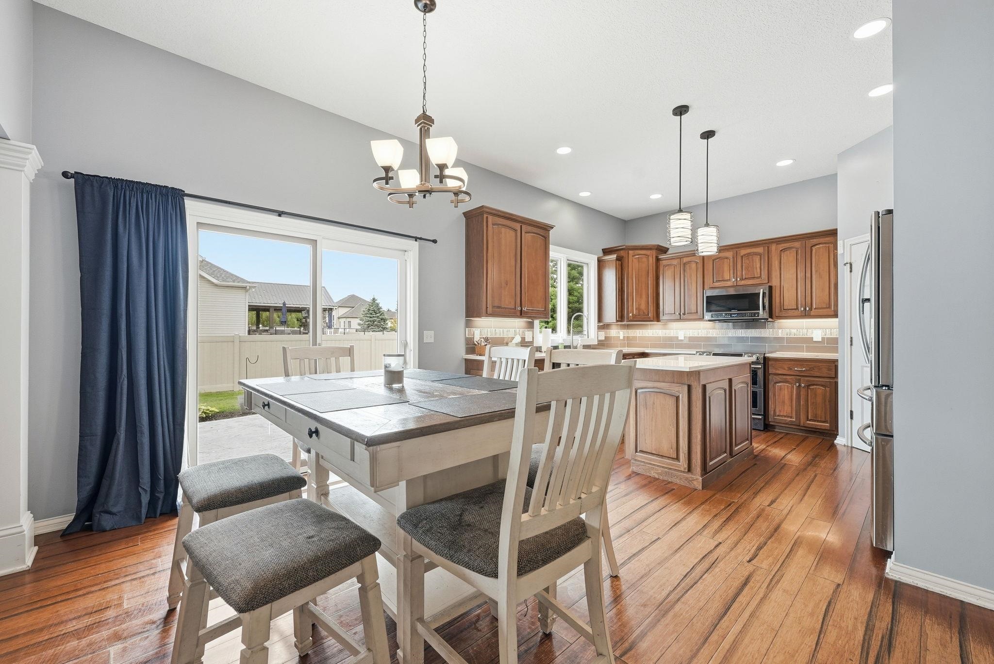 Open concept kitchen and dining area featuring wood-finish flooring, a kitchen island with pendant lighting, solid wood cabinetry, stainless steel appliances, and a tiled backsplash