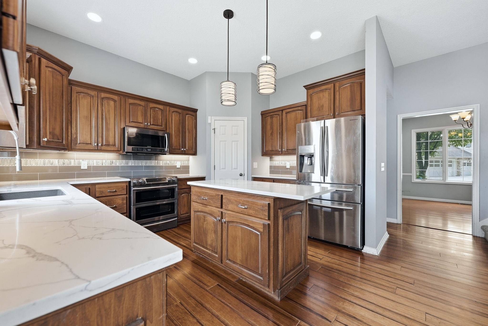 Well-appointed kitchen featuring wood cabinetry, stainless steel appliances, white countertops, a tiled backsplash, and wood-finish flooring