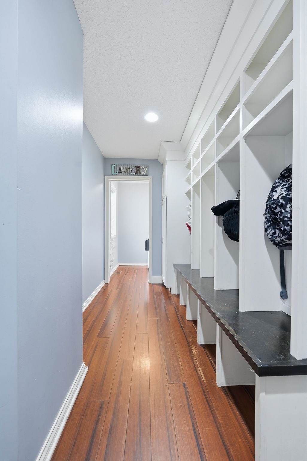 Hallway featuring wood-finish flooring, a built-in storage bench with individual cubbies, recessed lighting, and light blue wall paint