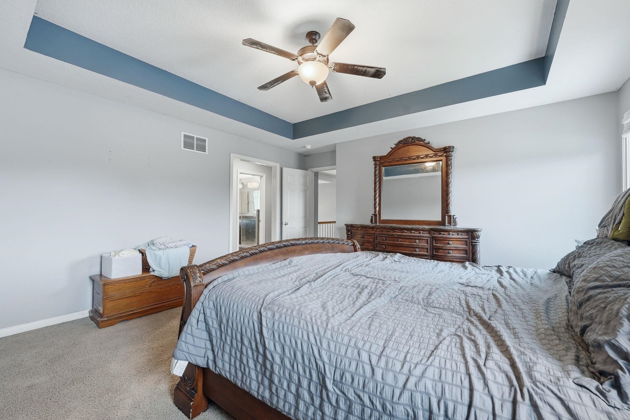 Recessed tray ceiling with a ceiling fan, carpeted flooring, and a doorway leading to an interior space