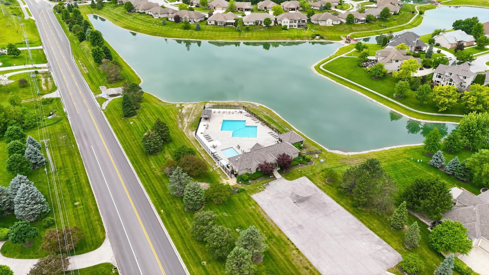Aerial perspective showcasing a residential community with a large body of water, a central building with a swimming pool, and surrounding properties