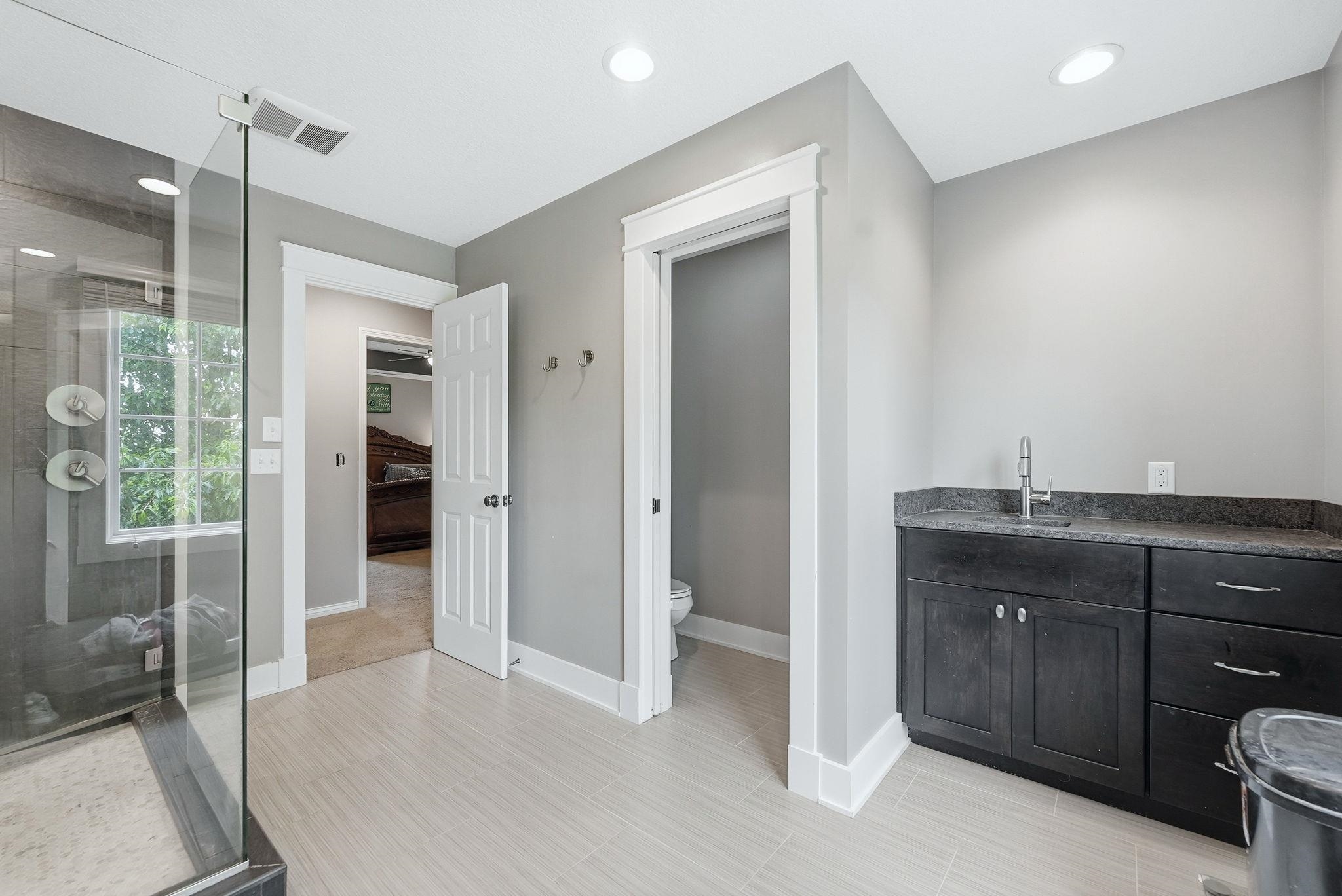 Spacious bathroom featuring a glass-enclosed shower, light-toned tile flooring, and a vanity with a dark countertop and cabinetry