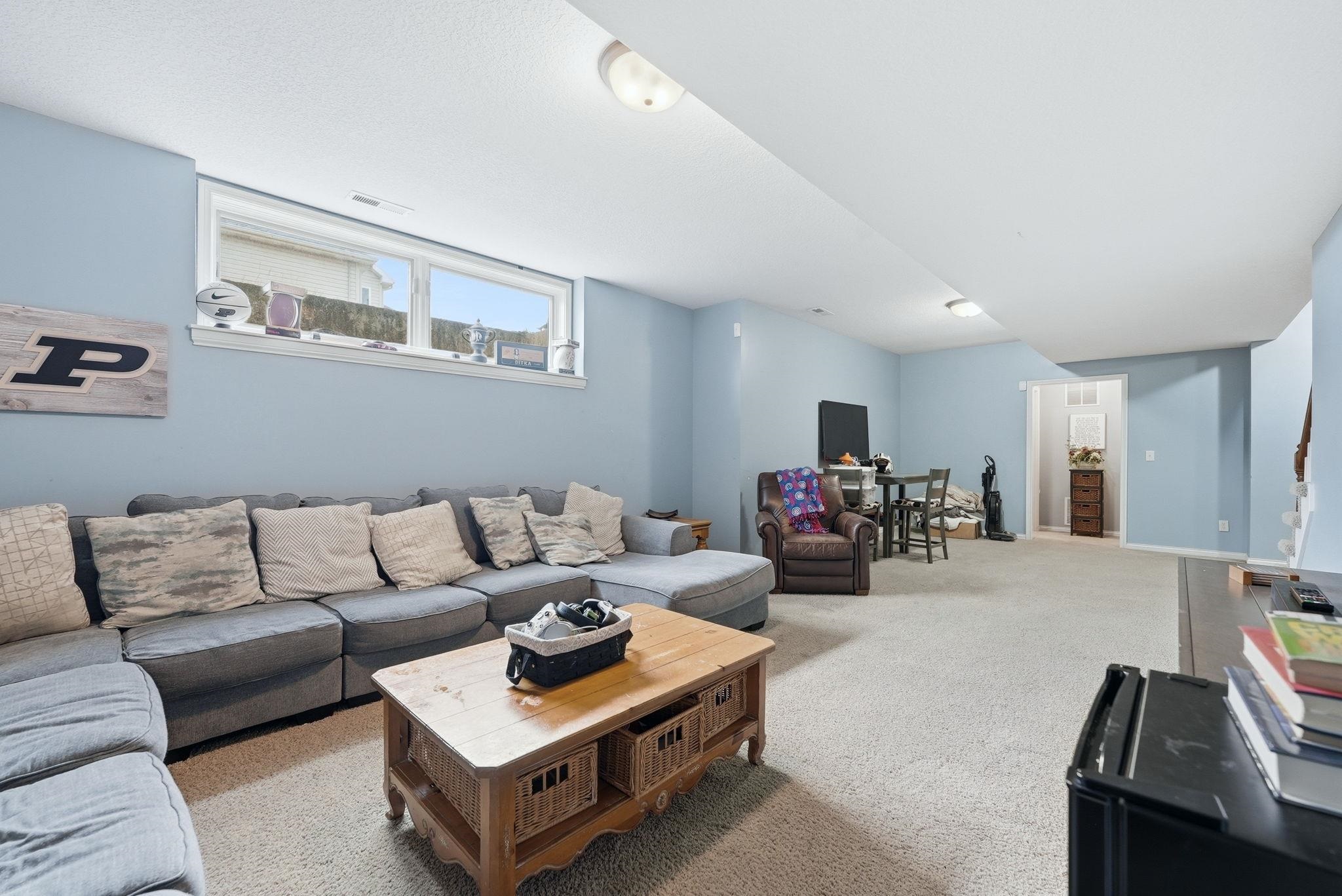 Spacious lower-level living area with light blue walls and neutral carpet flooring