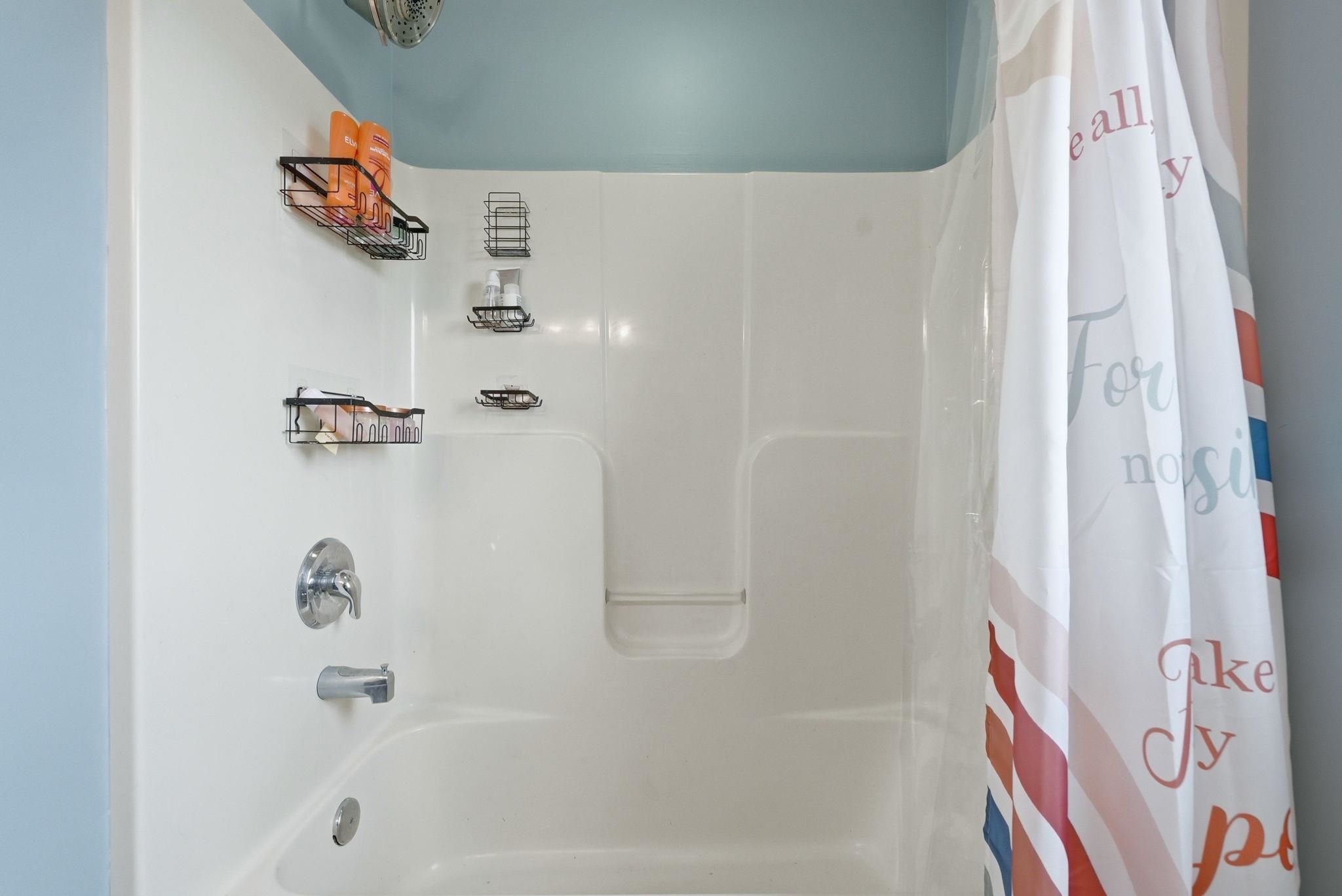 White acrylic tub and shower combination featuring chrome fixtures and a fixed showerhead
