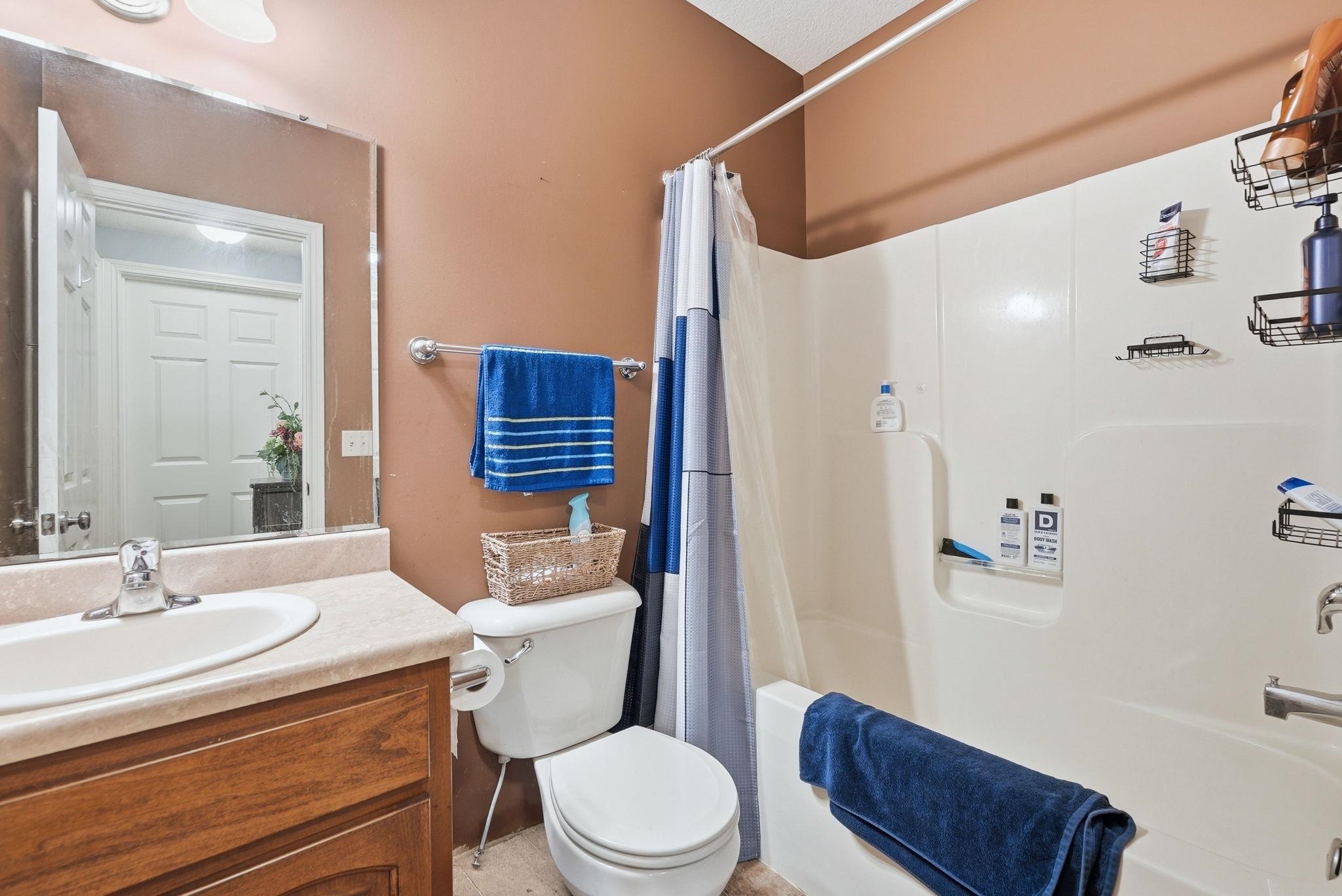 Full bathroom featuring a single vanity with wood-finish cabinetry and an integrated sink, a large wall-mounted mirror, and a toilet