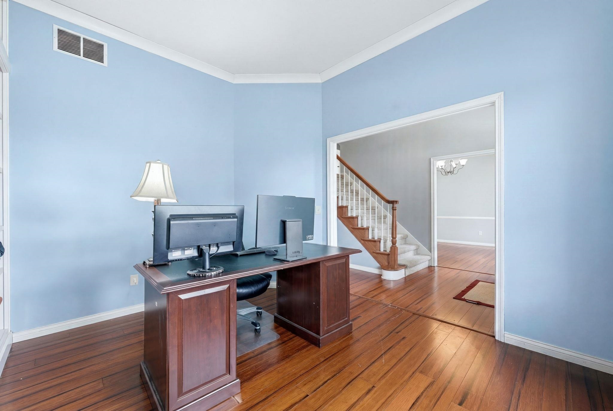 Room featuring wood-finish flooring, light blue walls, white crown molding, and a white baseboard trim
