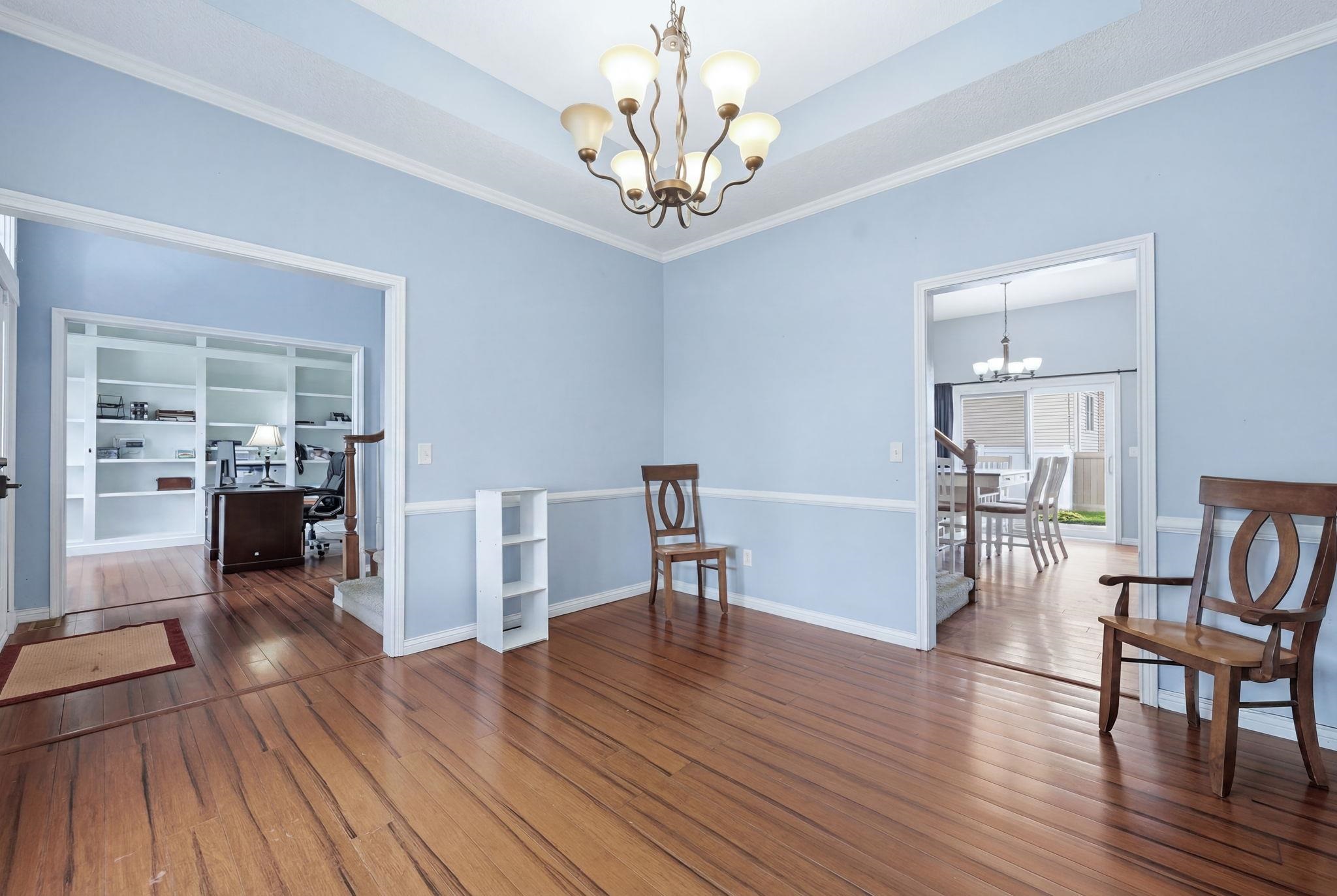 Spacious room featuring wood-finish flooring, a tray ceiling with a chandelier, and light blue walls with white wainscoting