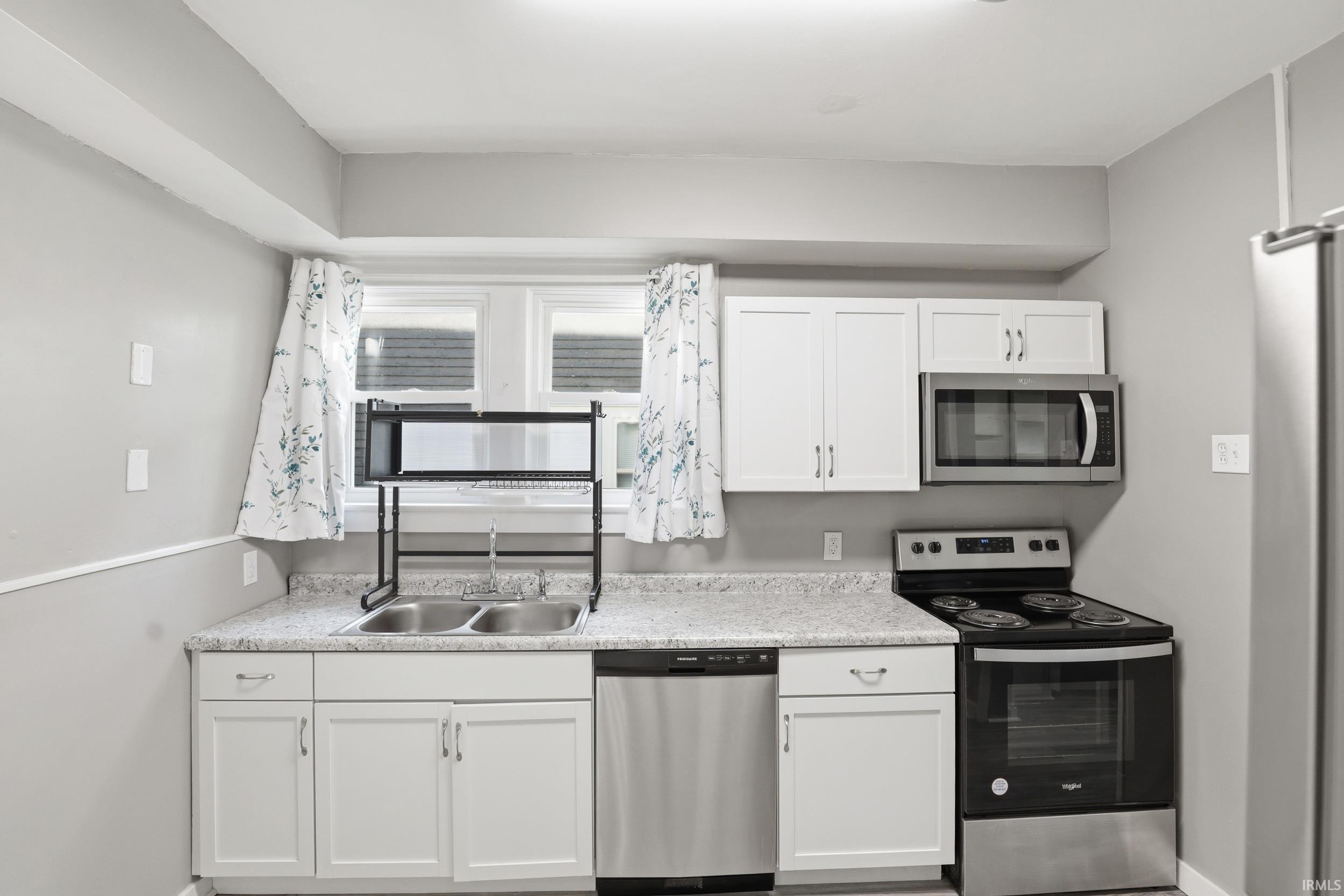 Kitchen featuring white cabinetry, light-colored countertops, a double basin sink, stainless steel dishwasher, and a black and stainless steel range