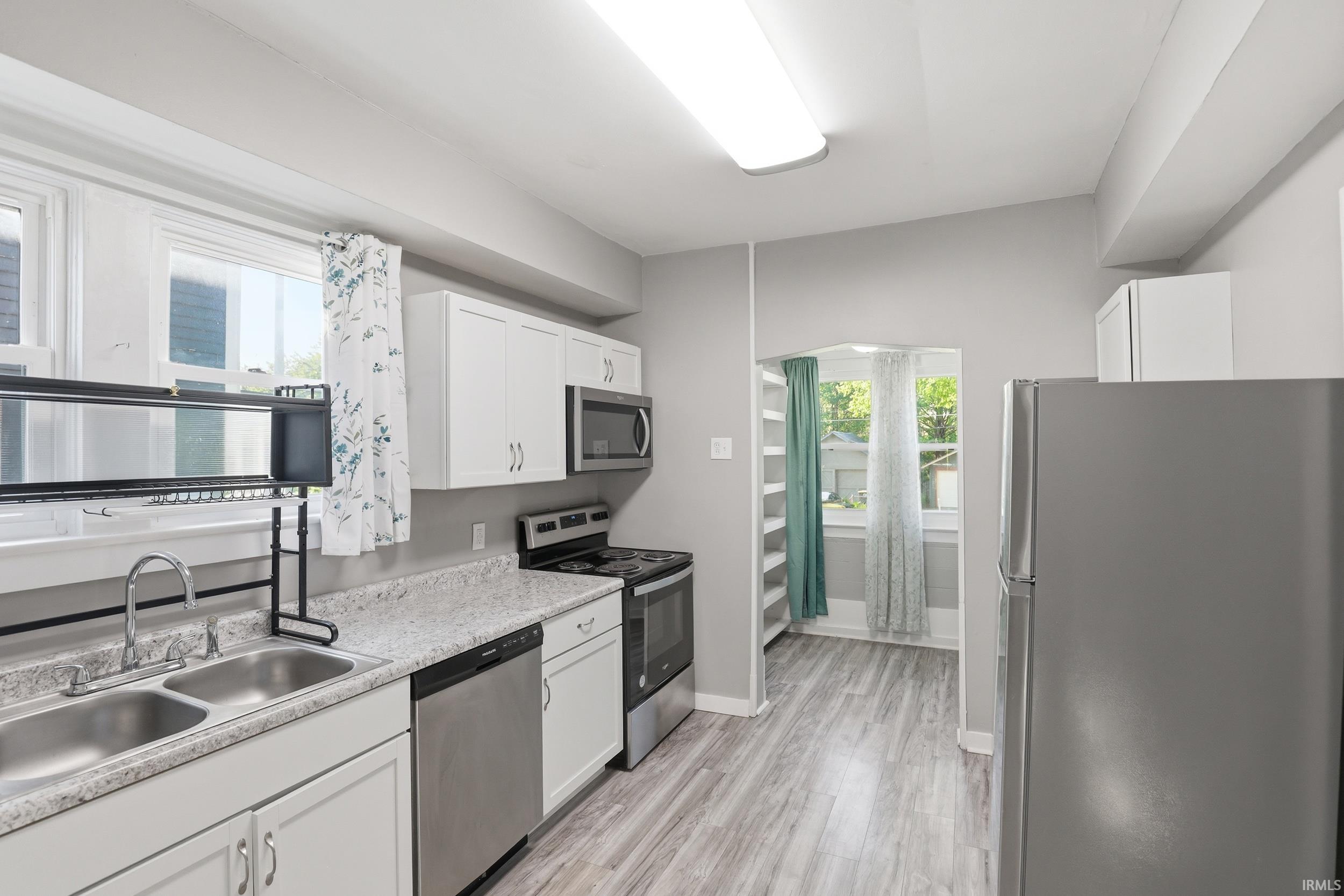 Kitchen featuring white cabinetry, light-toned countertops, a stainless steel double basin sink, and wood-finish flooring