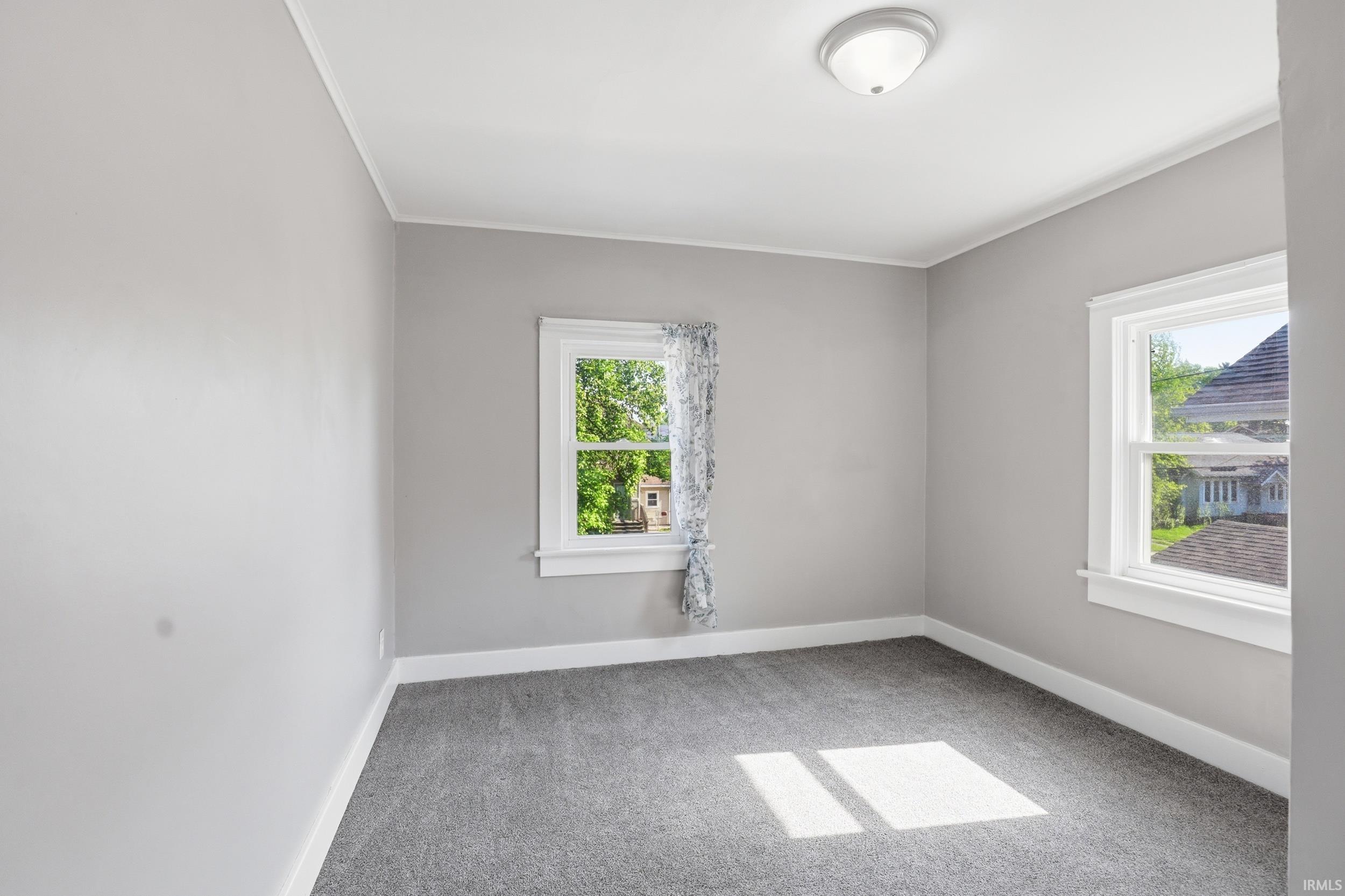 Room featuring light gray painted walls, gray carpeting, two white-trimmed windows, and a flush-mount ceiling light fixture