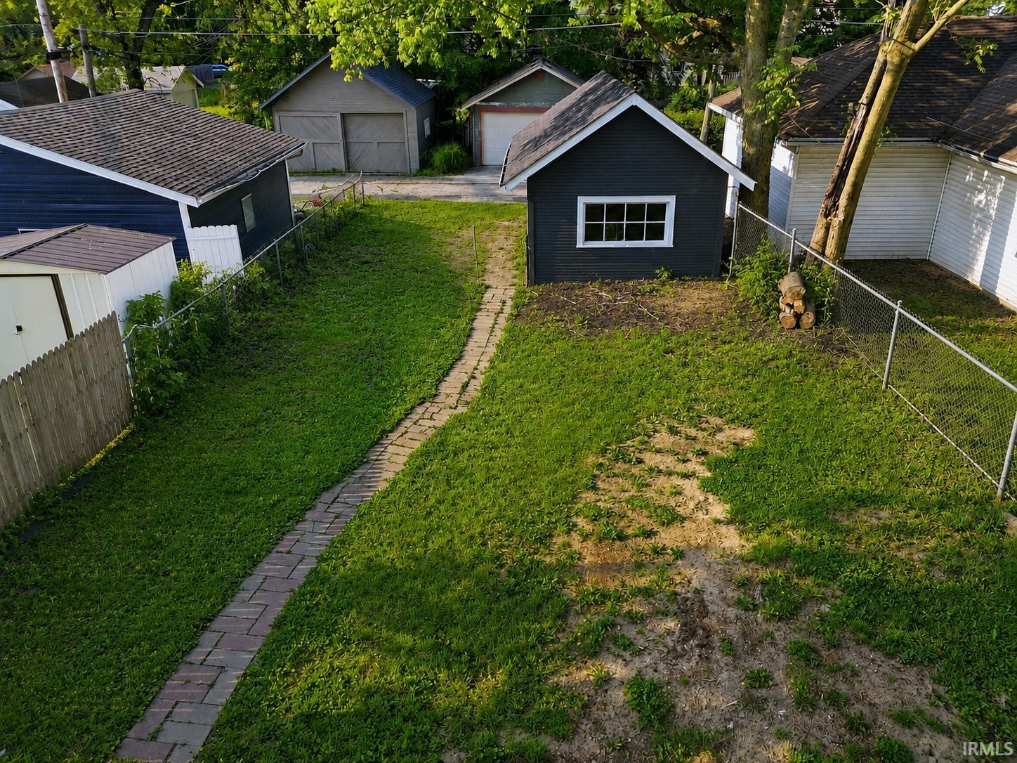 Spacious rear yard featuring a brick paver pathway, chain-link fencing, and a detached shed with a single window