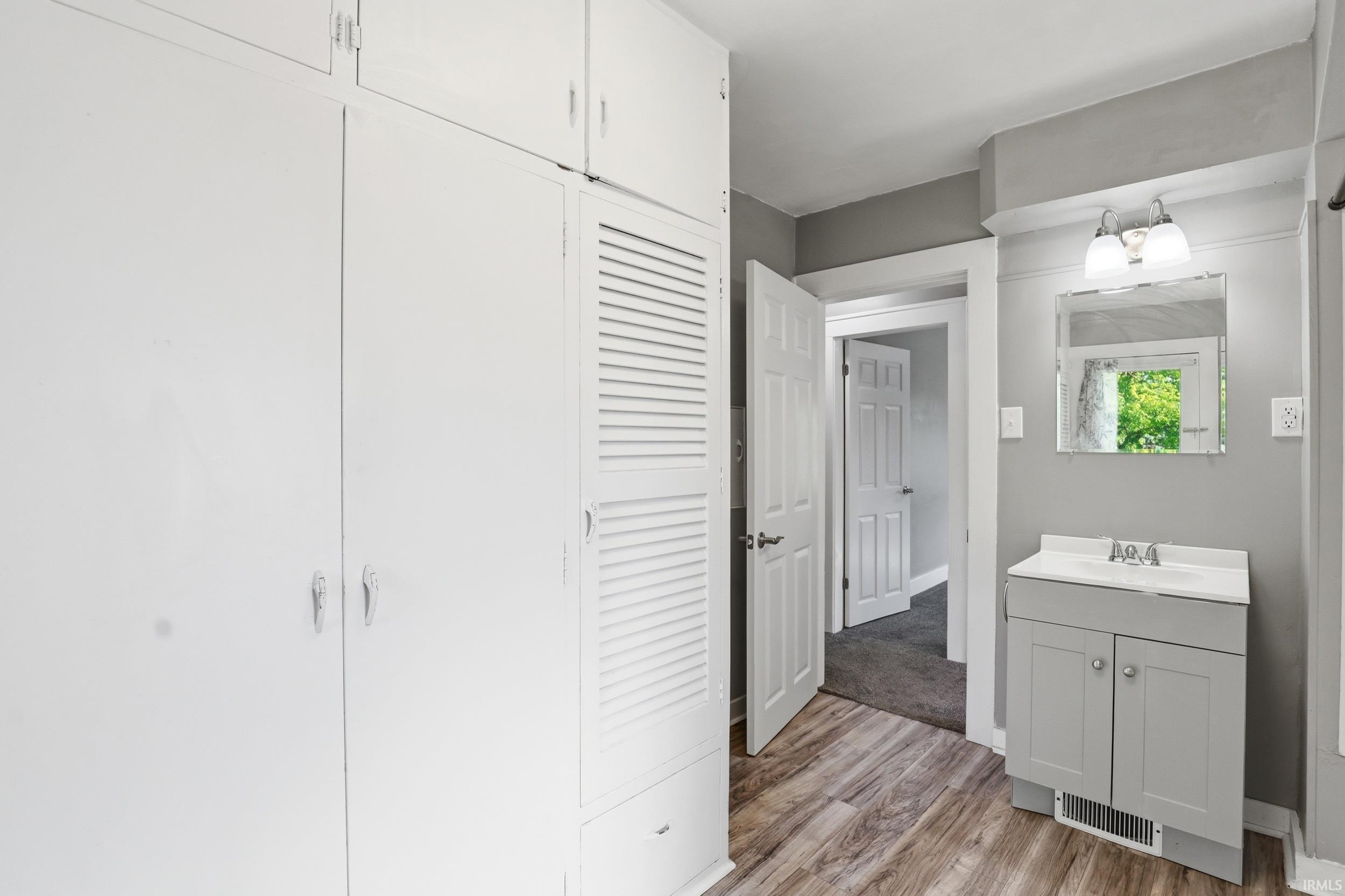 Built-in white cabinetry with louvered accents, a gray vanity with a white sink, and wood-finish flooring