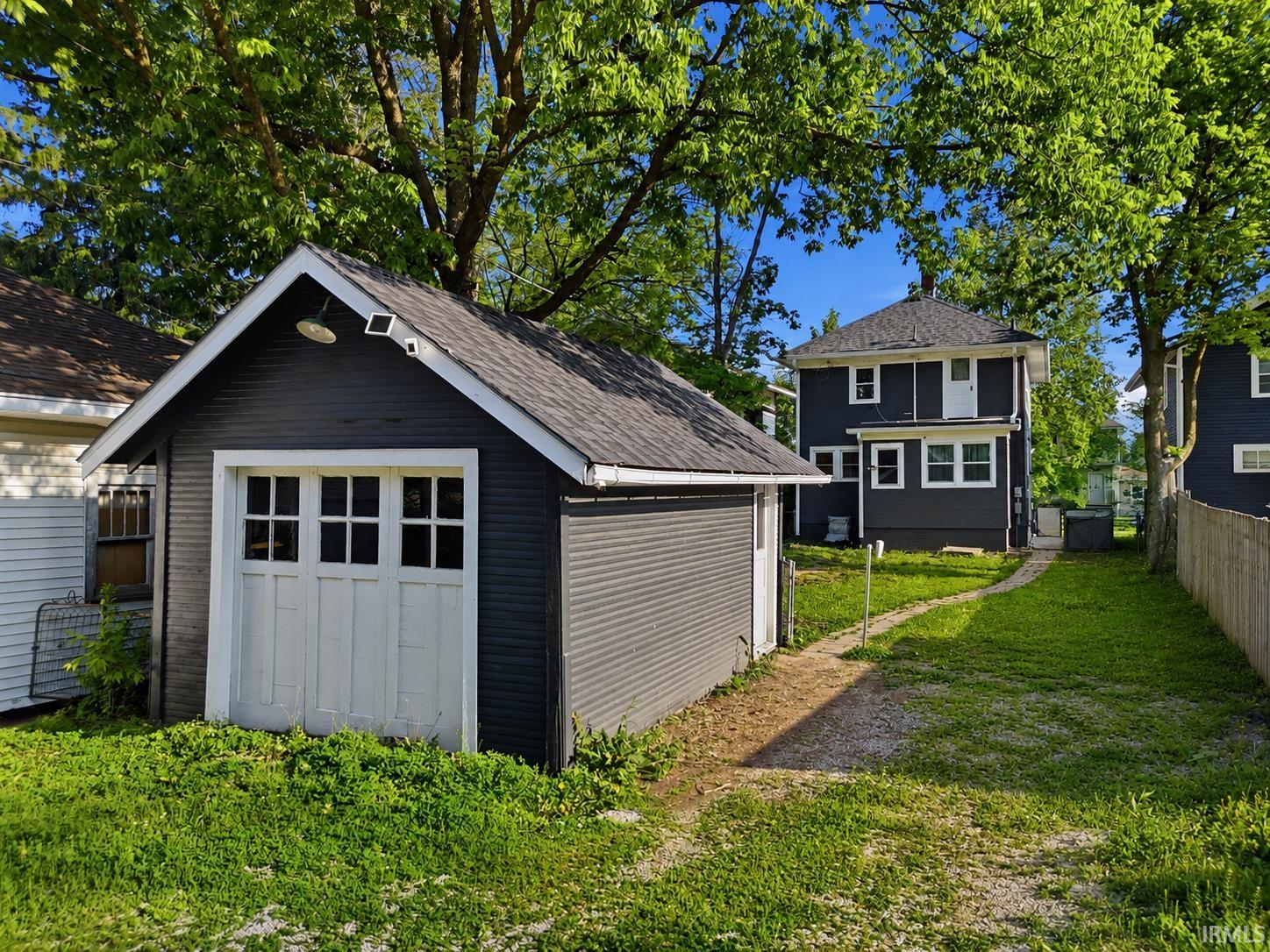 Detached garage featuring a white paneled door with window inserts and dark siding, complemented by a gabled roof