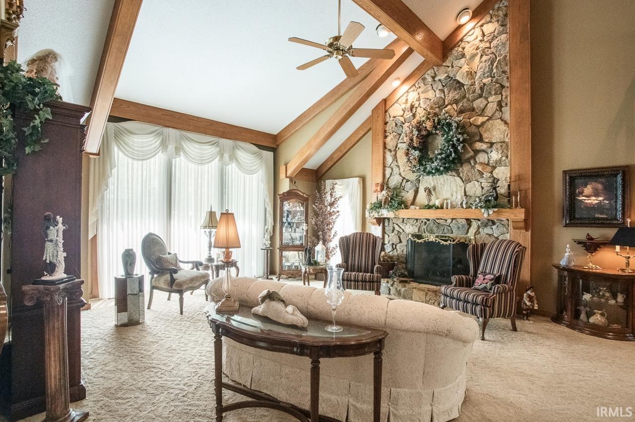 Vaulted ceiling with exposed wood beams, a stone fireplace with a wood mantel, floor-to-ceiling windows with drapes, recessed lighting, and a ceiling fan
