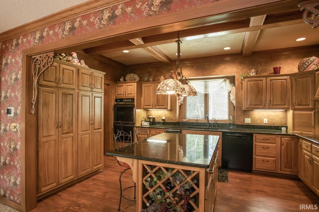 Kitchen featuring extensive wood cabinetry, granite countertops, a central island with integrated wine storage, double wall ovens, and wood-finish flooring