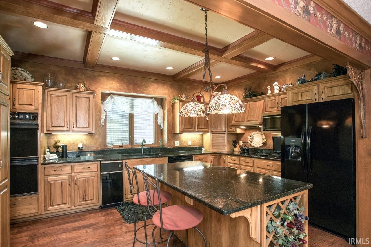 Kitchen featuring wood-finish flooring, wood cabinetry, dark countertops, a central island with integrated wine rack, and recessed lighting