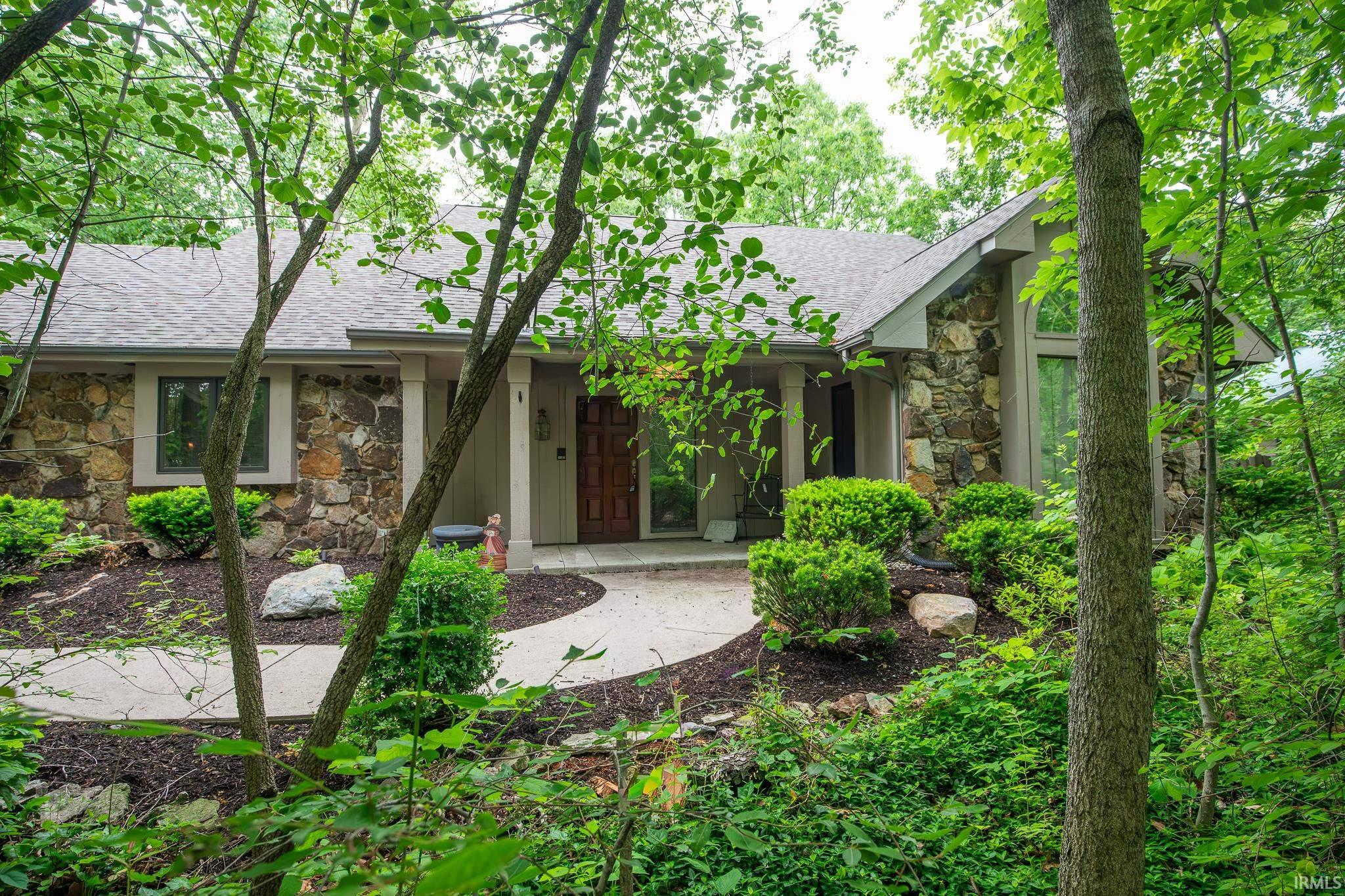 Stone and stucco exterior featuring a gabled roofline, front entry with a wood door, and a curved concrete walkway