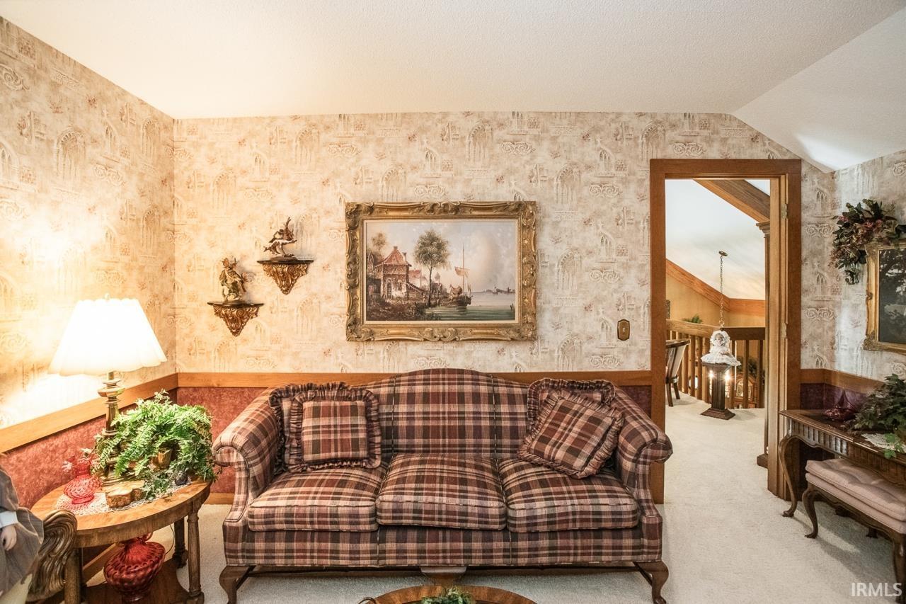 Carpeted room featuring patterned wallpaper, wainscoting, and a wood-trimmed doorway