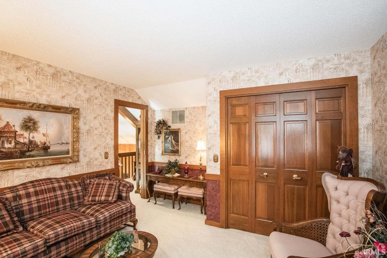 Carpeted room featuring paneled bifold closet doors, decorative wallpaper, and wood trim details