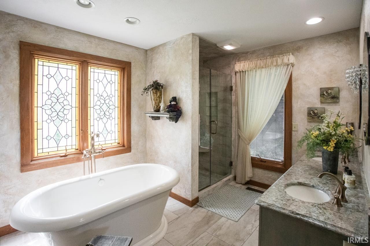 Freestanding soaking tub with a floor-mounted faucet, complemented by a stained-glass window feature and wood-finish trim