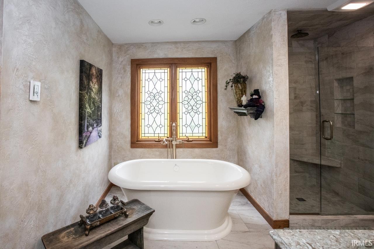 Freestanding soaking tub with floor-mounted fixtures, set against a stained glass window with wood trim