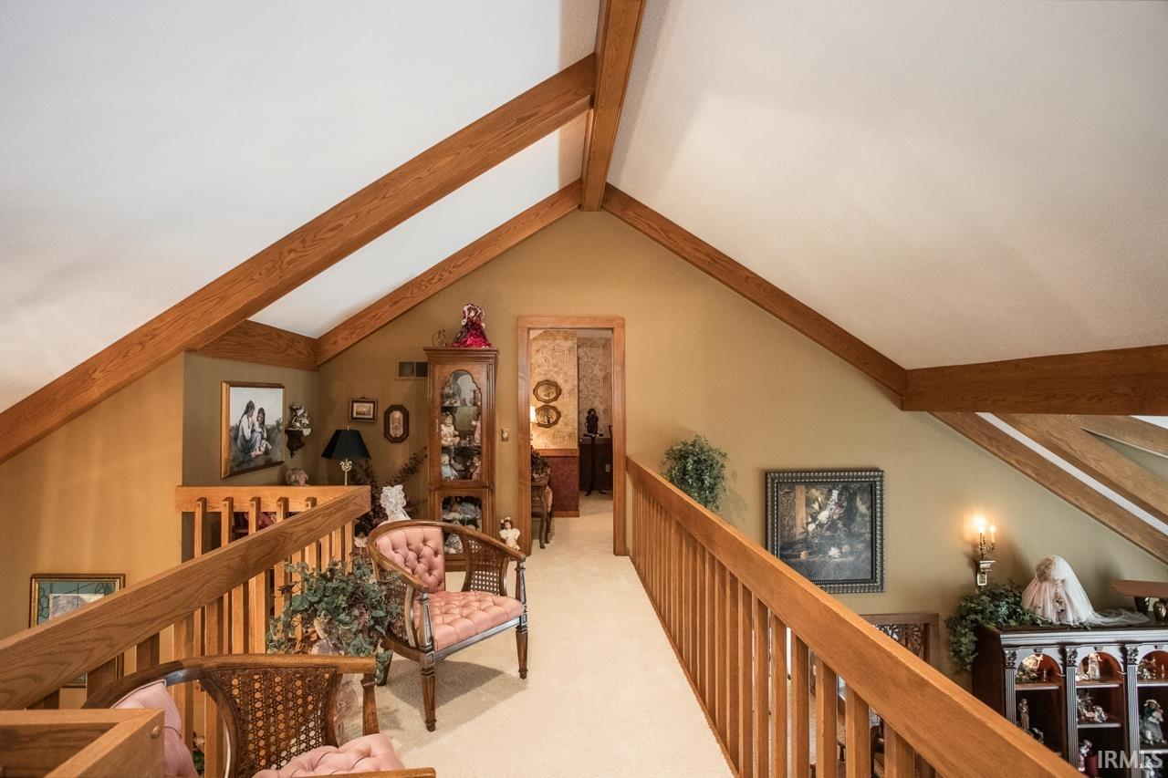 Vaulted ceiling with exposed wood beams, wood railing, and carpeted walkway