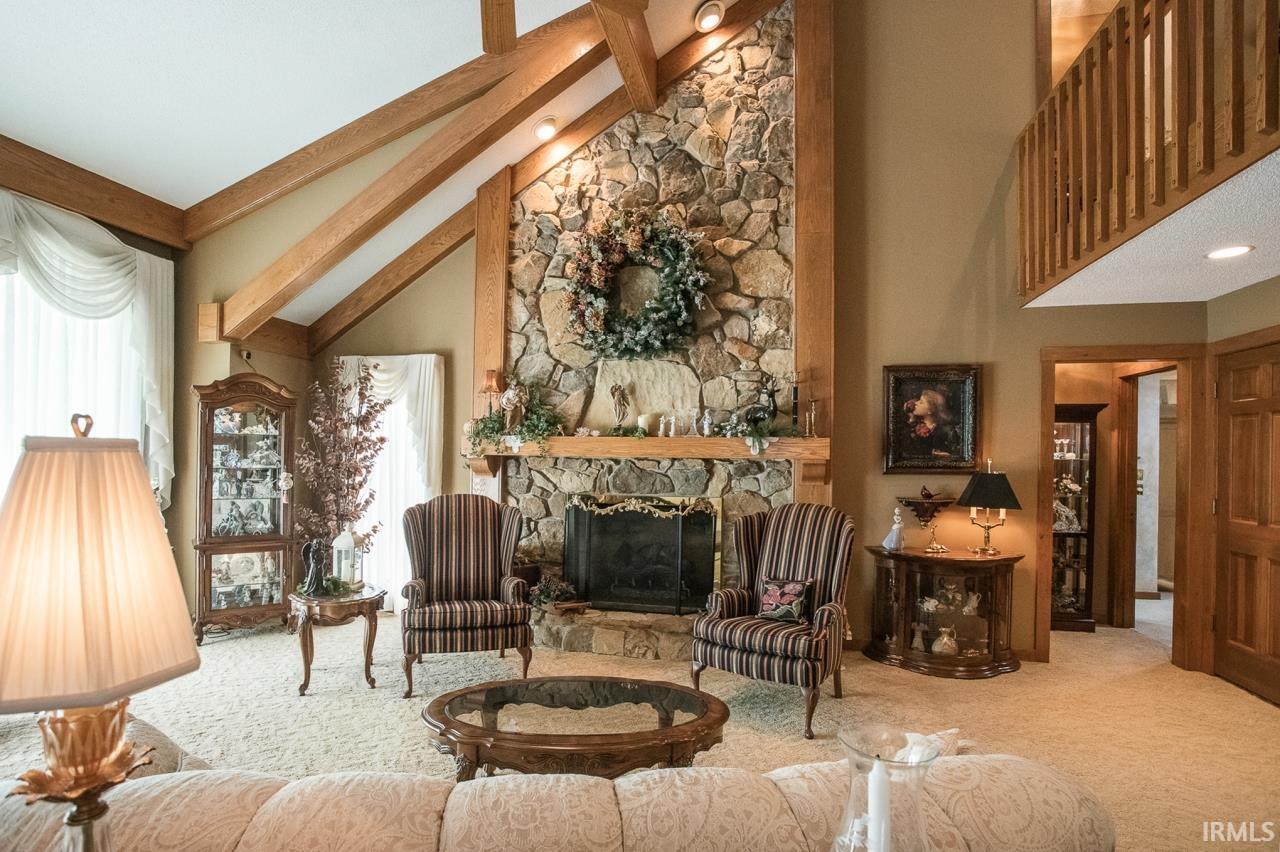 Vaulted ceiling featuring exposed wood beams, a floor-to-ceiling stone fireplace, and a wood mantel