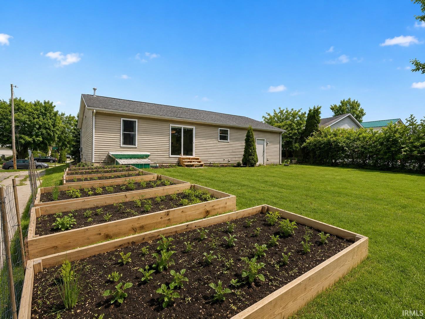 Expansive backyard featuring multiple raised garden beds, a manicured lawn, and a light-toned siding exterior with sliding glass door access
