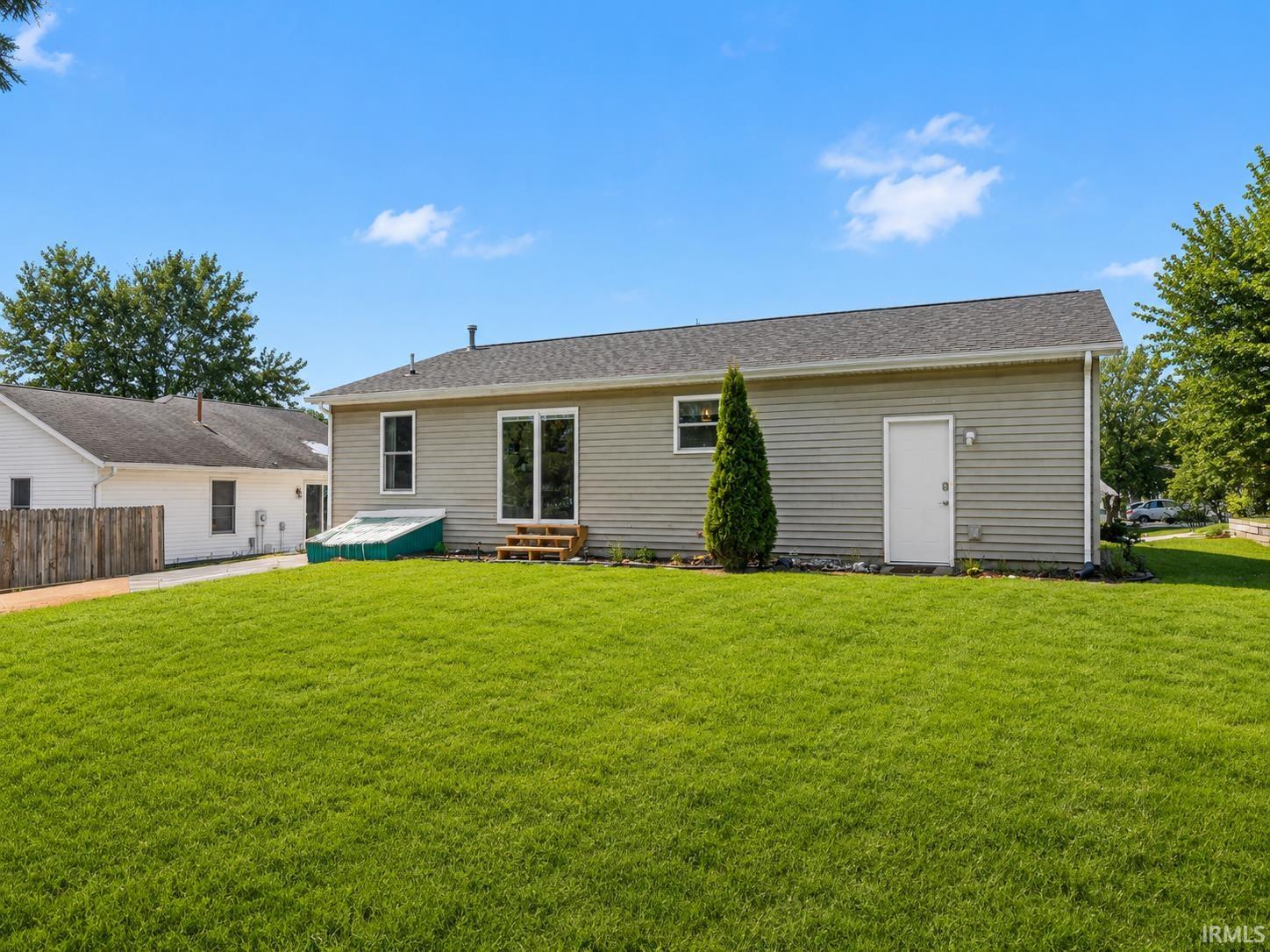 Expansive backyard featuring a manicured lawn, vinyl siding, a rear entry door, and a sliding glass door leading to a wooden deck