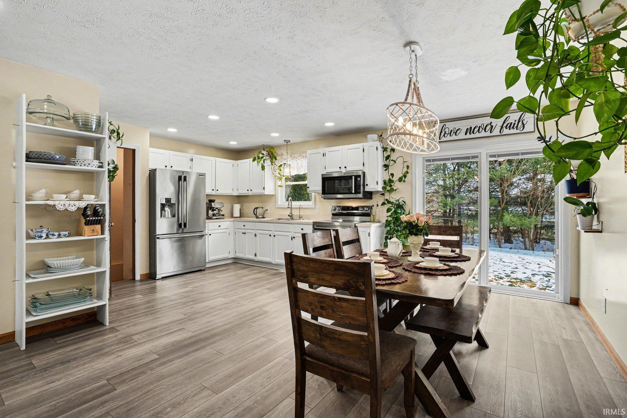 Open-concept kitchen and dining area featuring light wood-finish flooring, white cabinetry, stainless steel appliances, and a sliding glass door