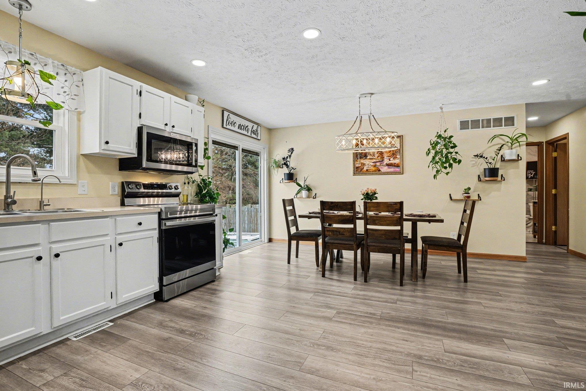 Open-concept kitchen and dining area featuring white cabinetry, stainless steel appliances, wood-finish flooring, and recessed lighting