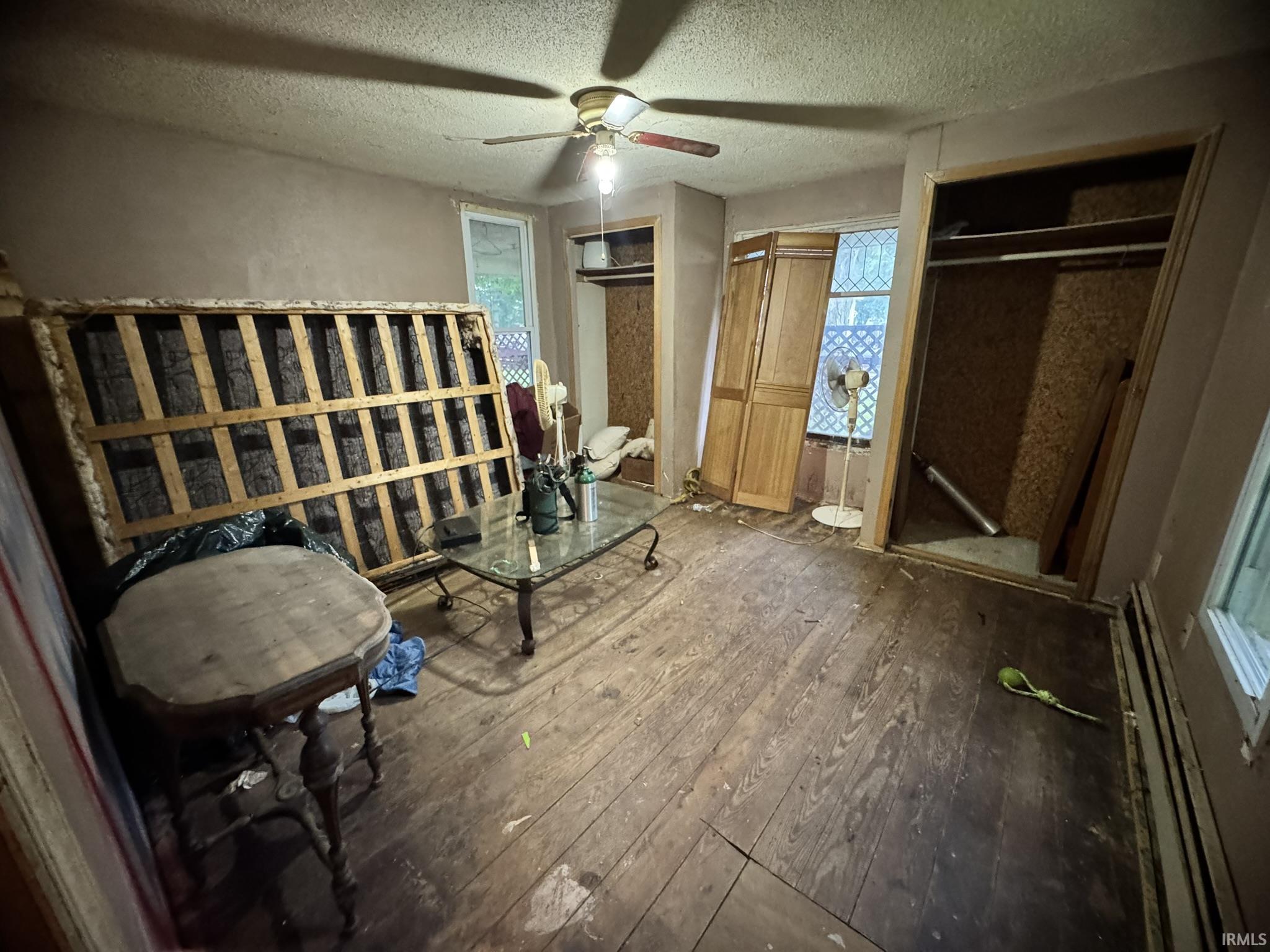 Room with wood-finish flooring, two window openings, and an exposed closet frame with a hanging rod