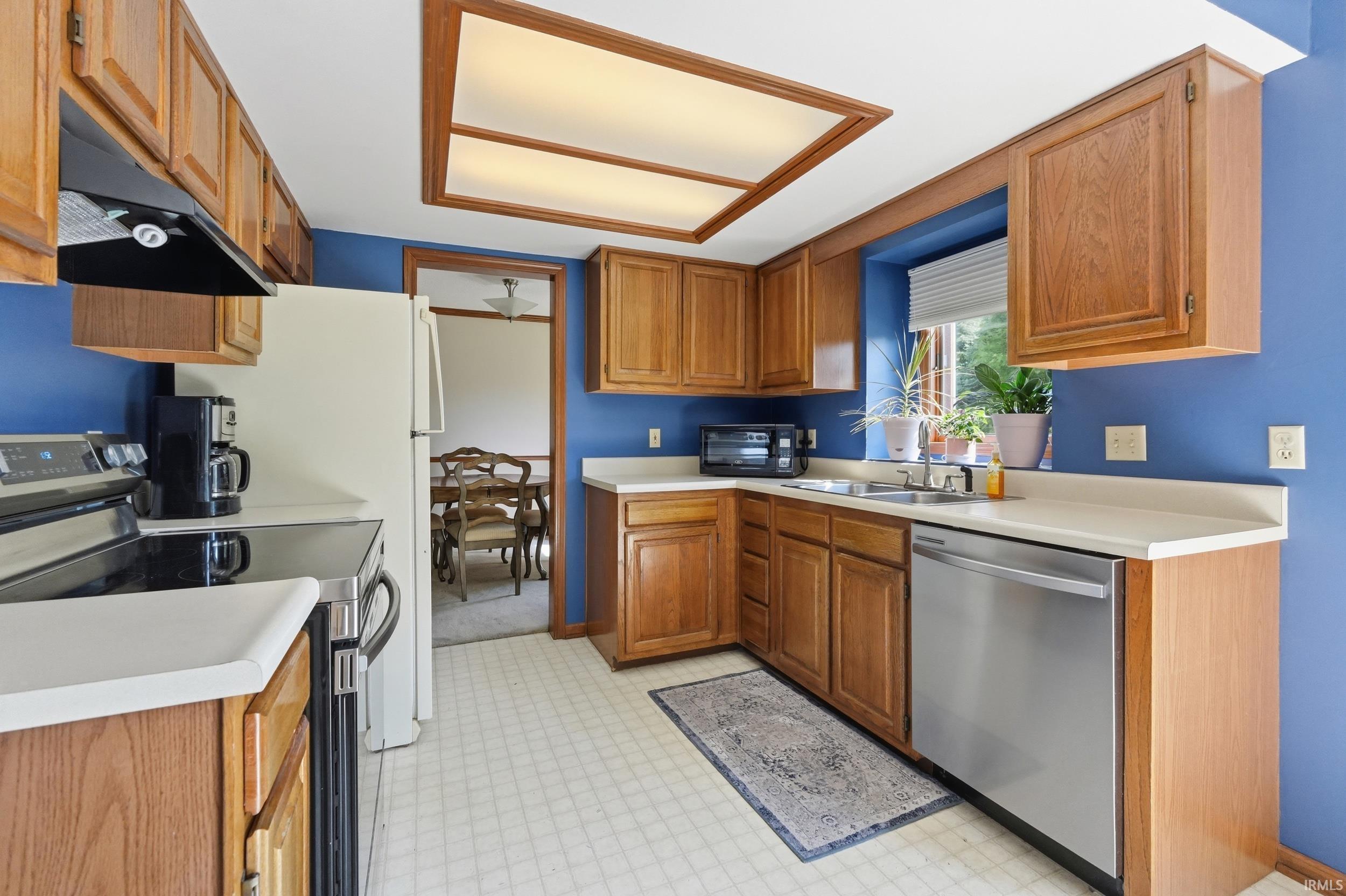 Kitchen featuring wood cabinetry, white countertops, stainless steel dishwasher, an electric range with overhead vent, and a window above the sink