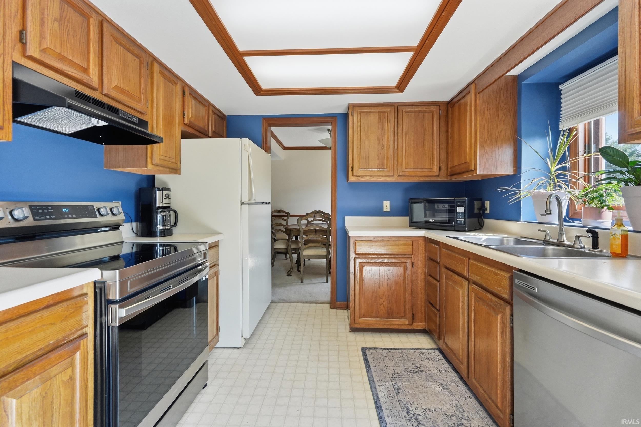 Kitchen featuring wood cabinetry, light countertops, stainless steel electric range, stainless steel dishwasher, and a window above the sink