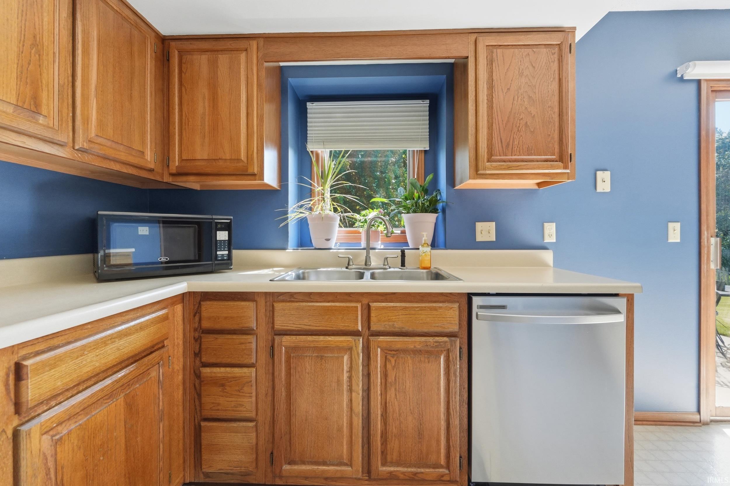 Kitchen featuring warm-toned wood cabinetry, light-toned countertops, and a double basin stainless steel sink