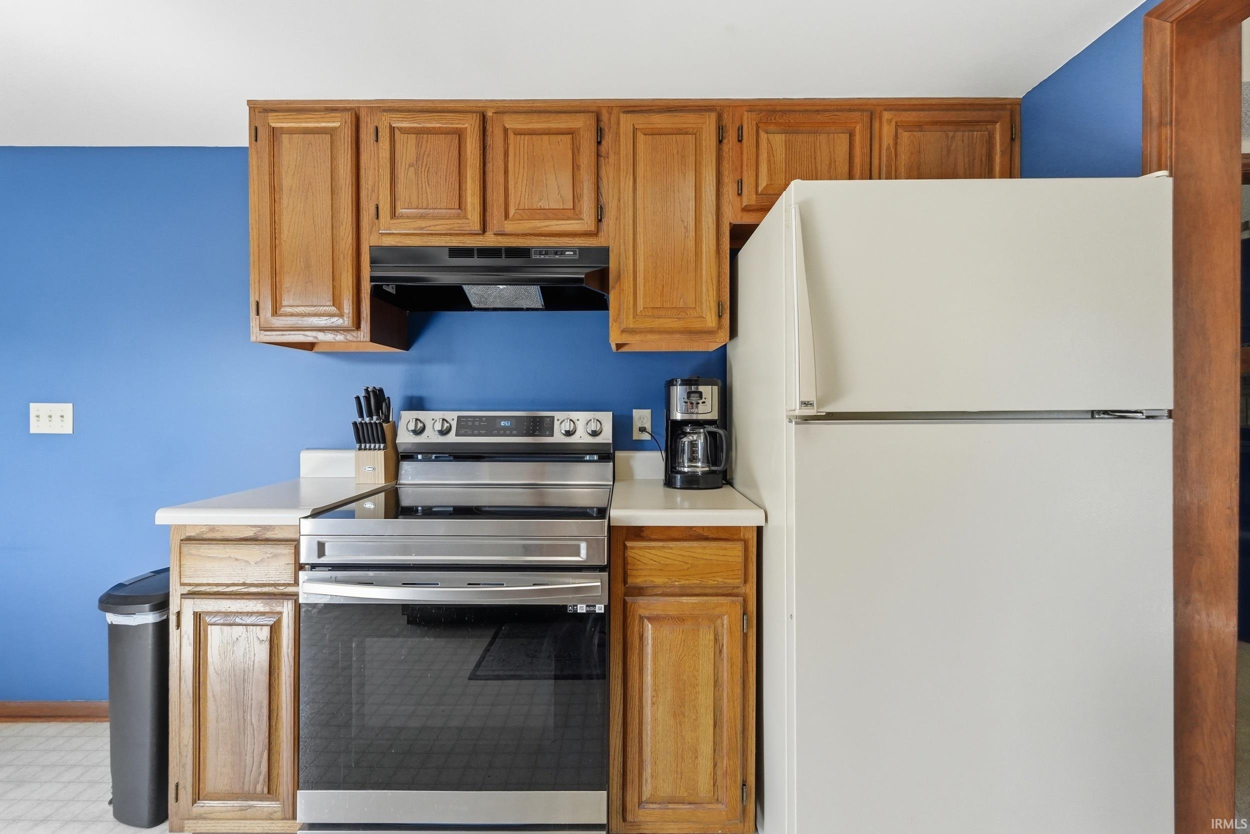 Kitchen featuring wood cabinetry, light countertops, and a full suite of appliances including a stainless steel range and a white refrigerator