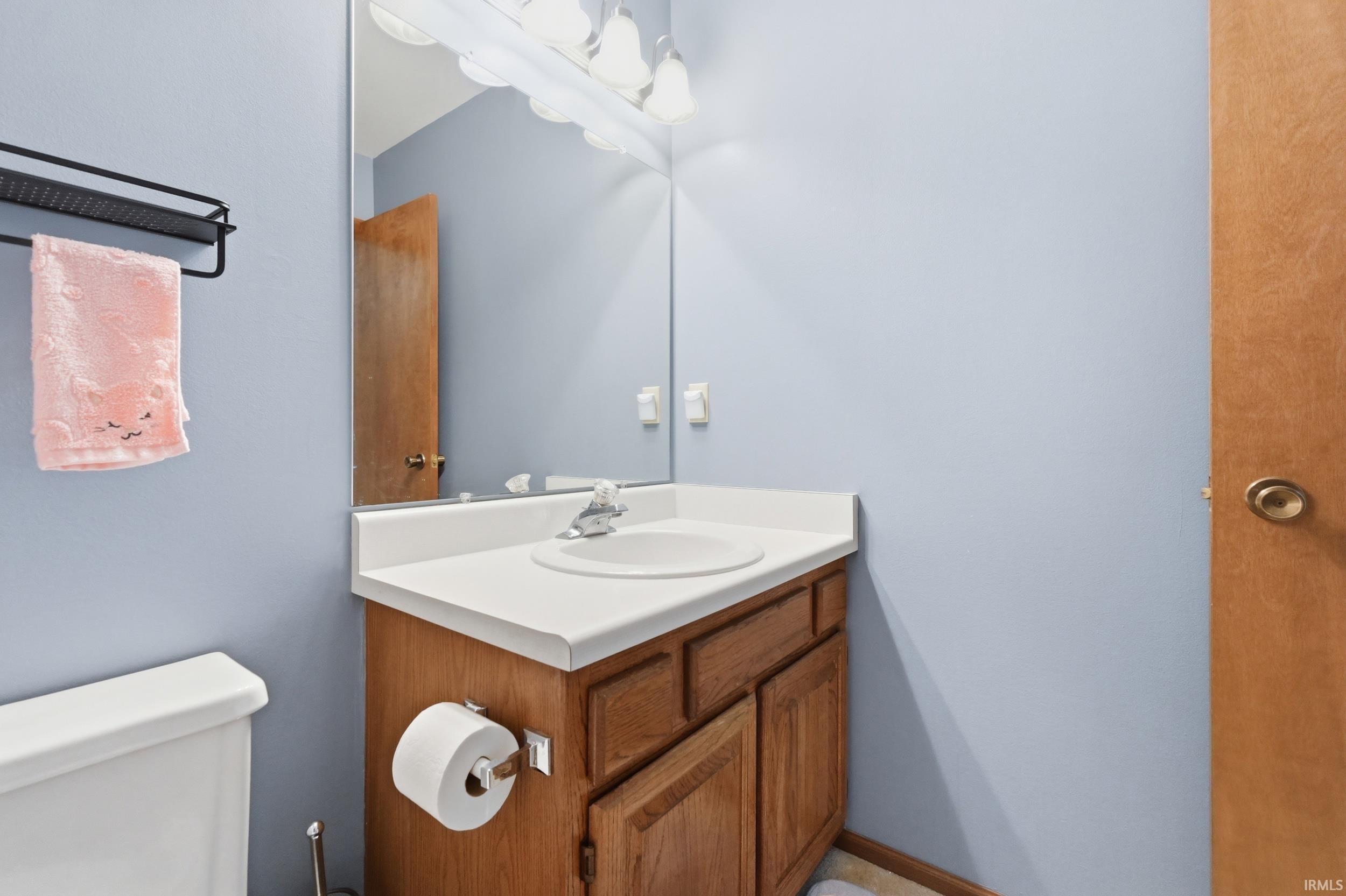 Bathroom vanity featuring a light wood-finish cabinet with white countertop, integrated sink, and an overhead mirror with vanity lighting