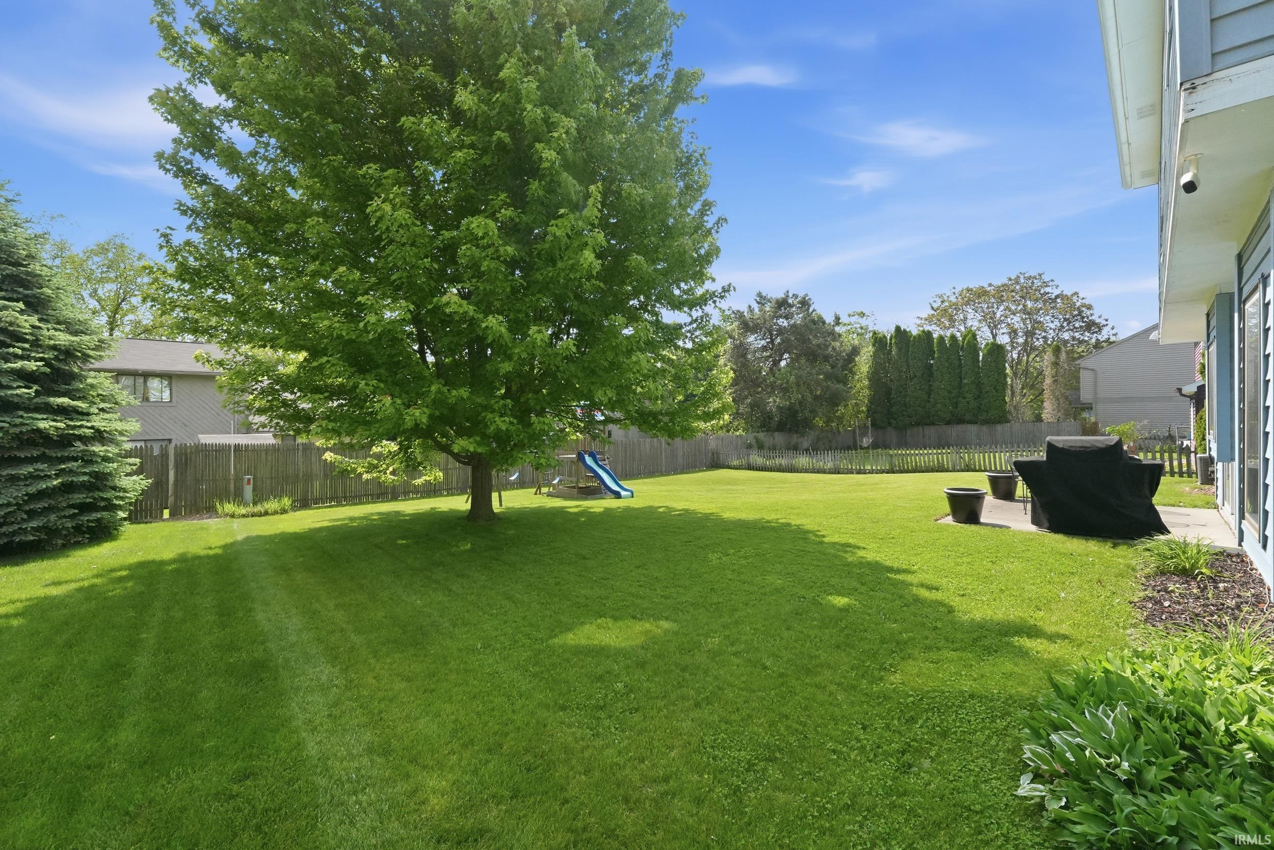 Expansive backyard featuring a large tree, a manicured lawn, a privacy fence, and a concrete patio