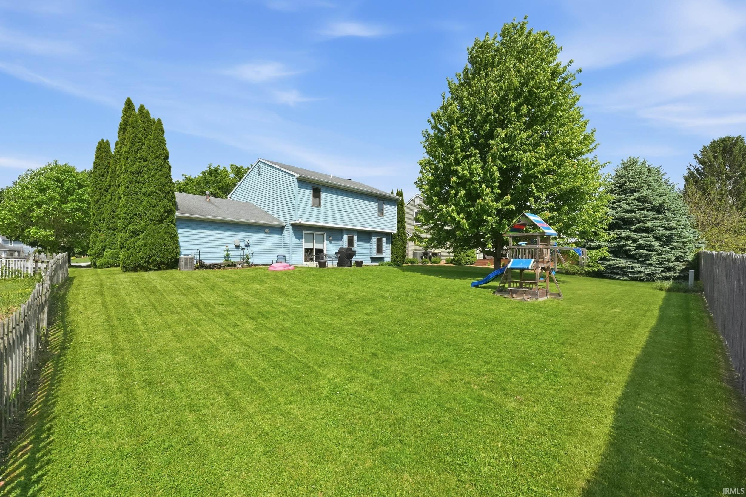 Expansive backyard featuring a lush lawn, mature trees, and a weathered picket fence