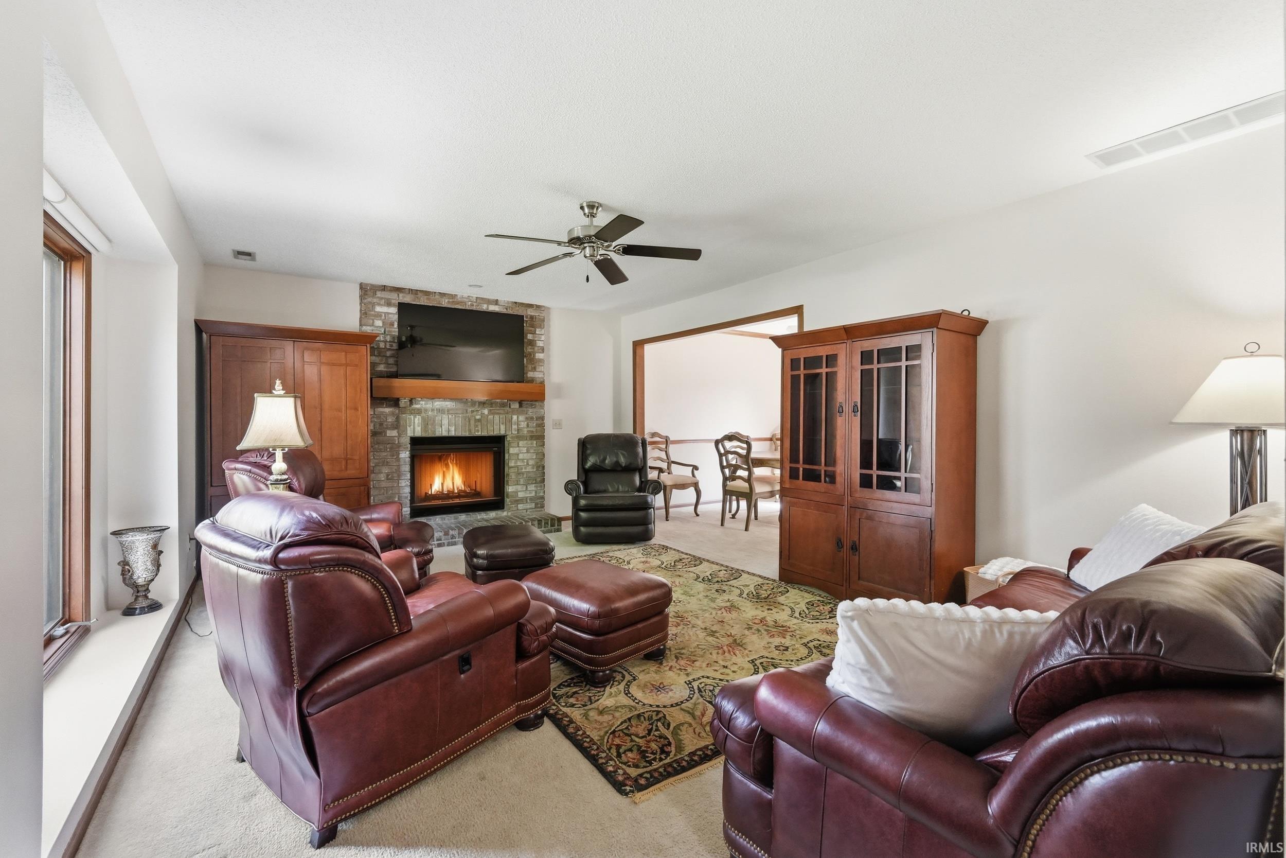 Spacious gathering room featuring a stone-faced fireplace with a wood mantle, ceiling fan, and large window sill