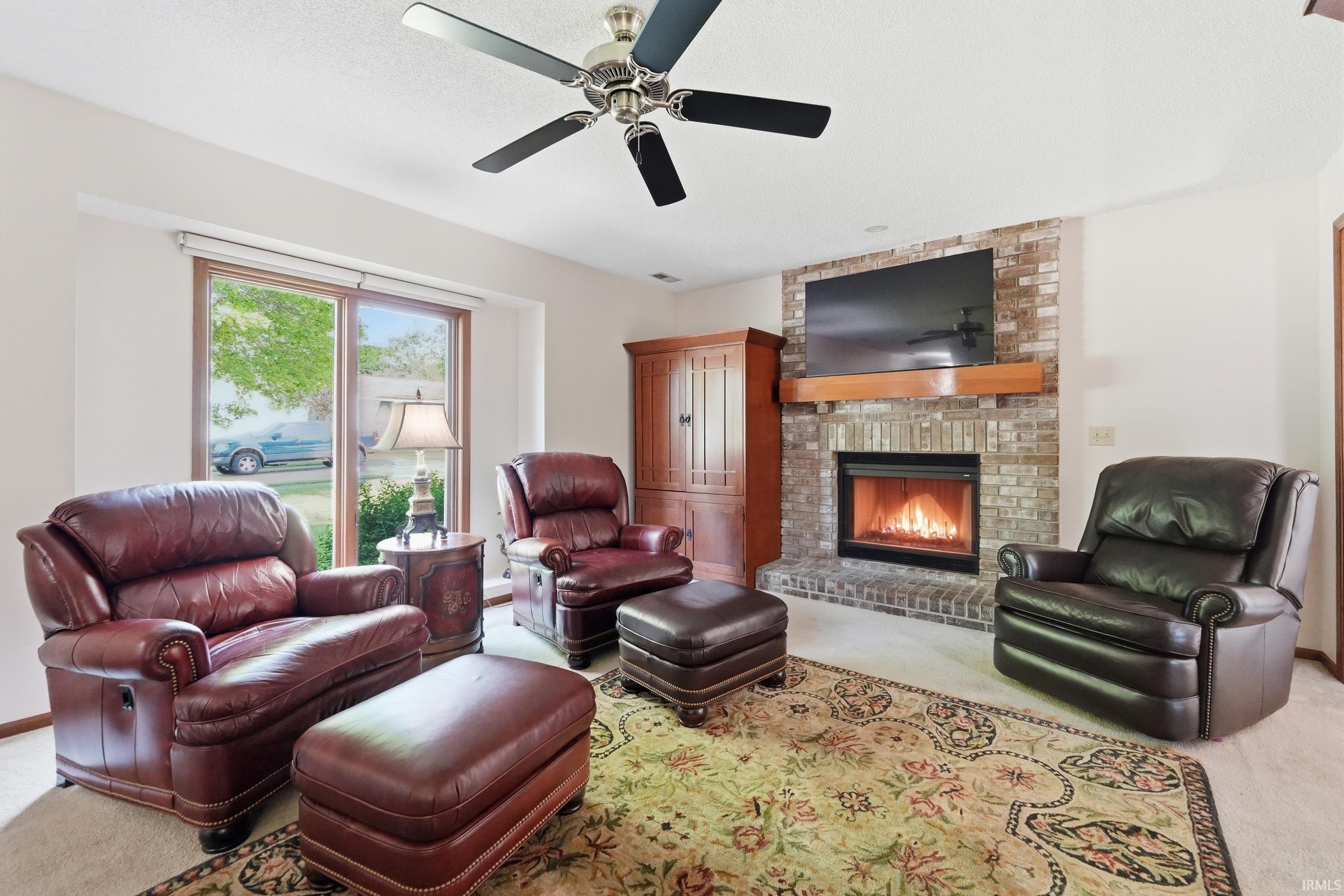 Living room featuring a brick-surround fireplace with a wood mantle, a ceiling fan, and sliding glass doors