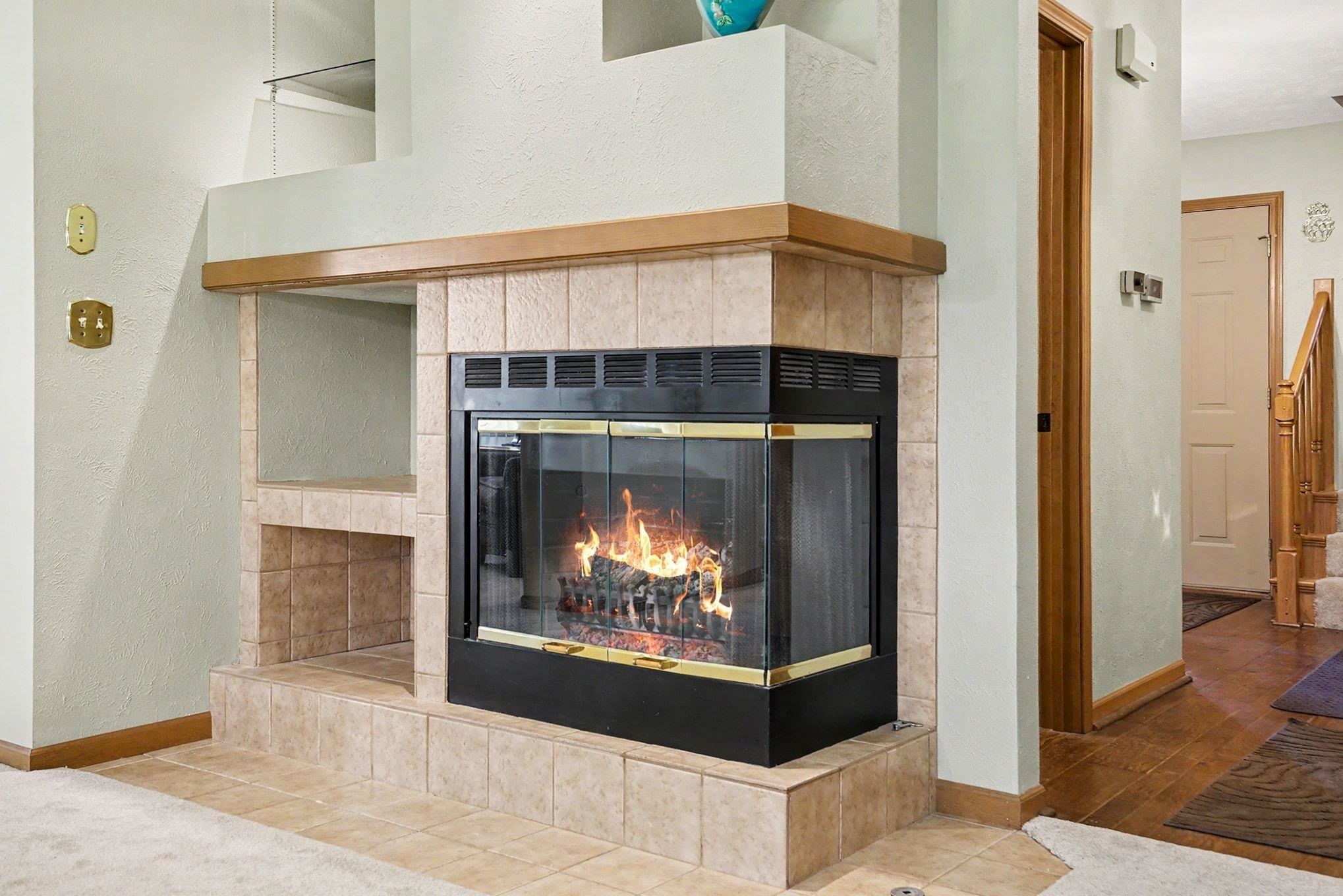 Corner fireplace with glass doors and tile surround, featuring a wood mantel