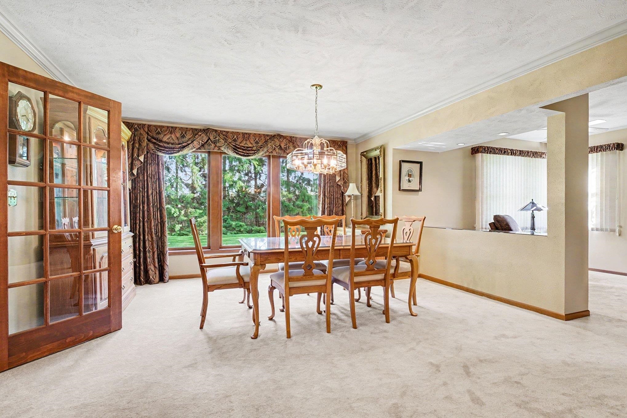 Formal dining space featuring a prominent crystal chandelier, extensive window views, plush carpeting, and a glass-paneled entry door