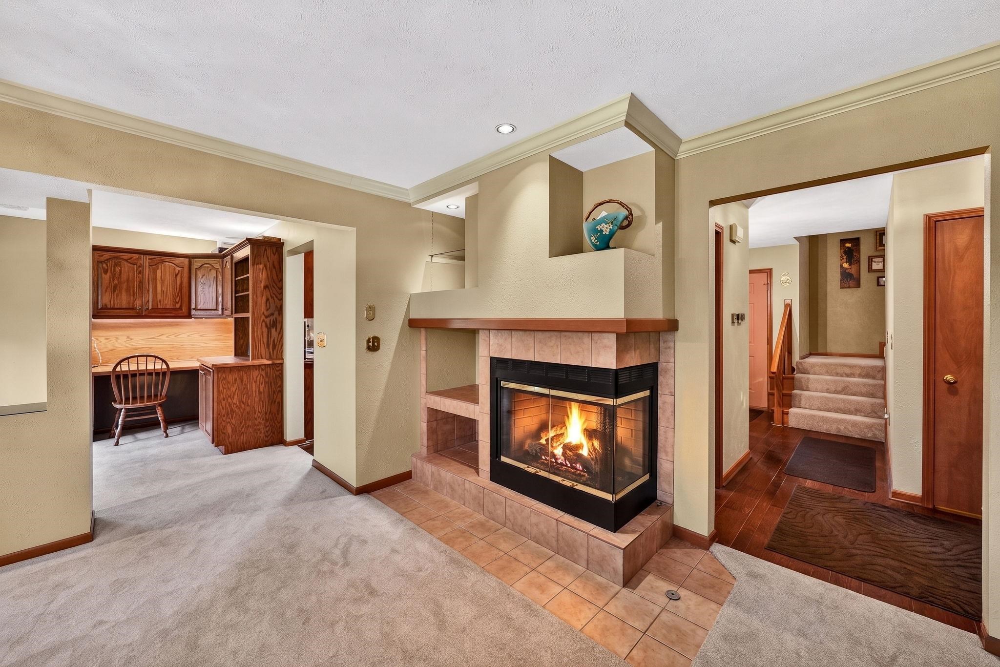 Corner fireplace with a tile hearth and integrated shelving, featuring crown molding, a built-in desk with wood cabinetry, and wood-finish flooring