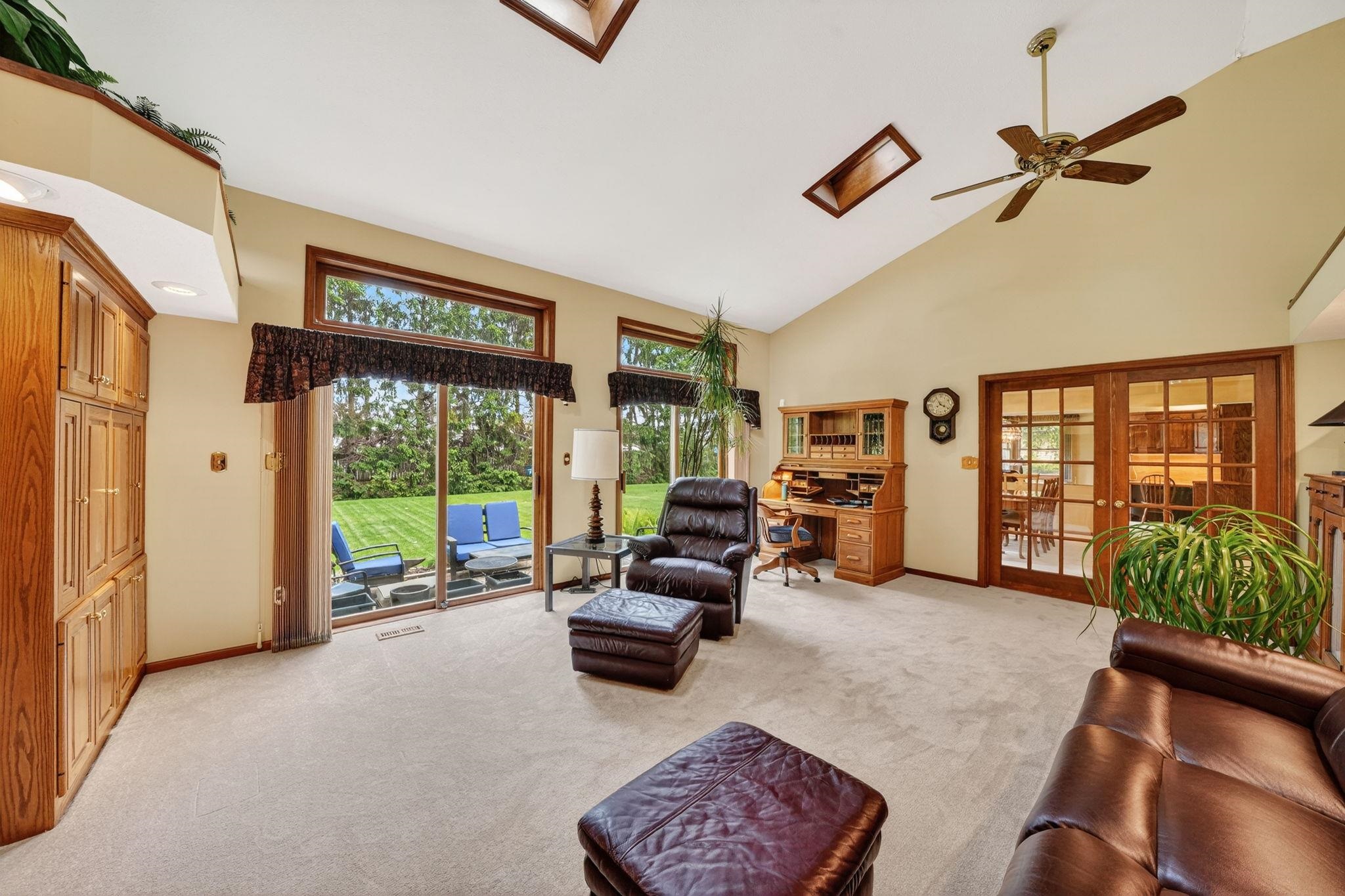 Spacious living area featuring a vaulted ceiling with skylights, light-colored carpeting, and a ceiling fan