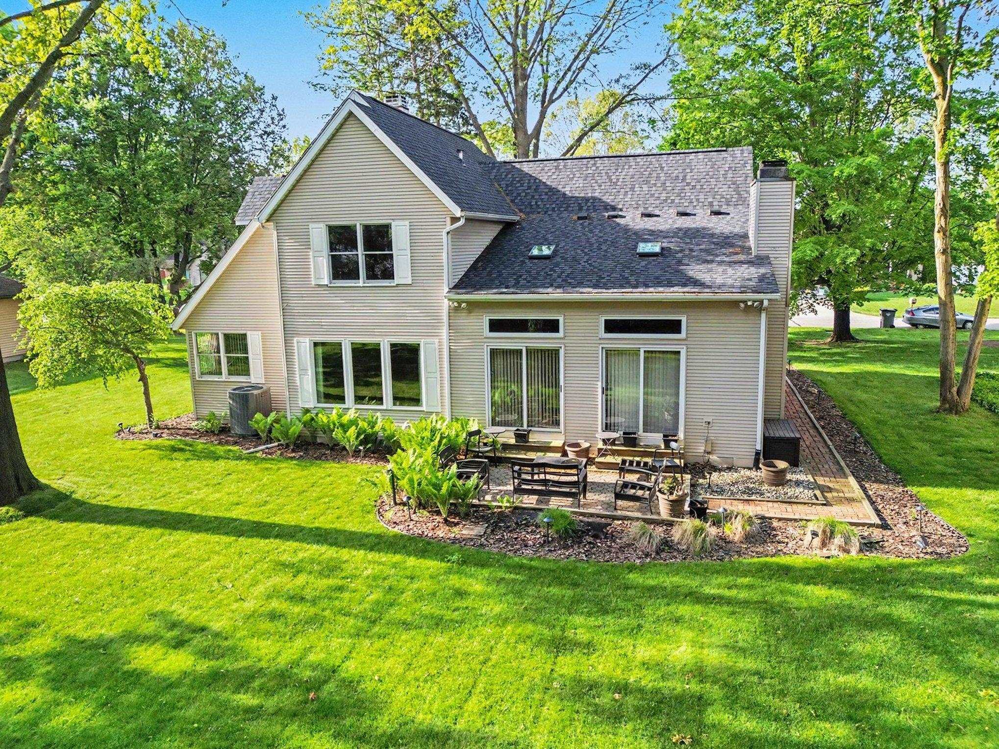 Rear exterior featuring a brick paver patio, sliding glass doors, multiple windows with white shutters, and a dark shingle roof with skylights